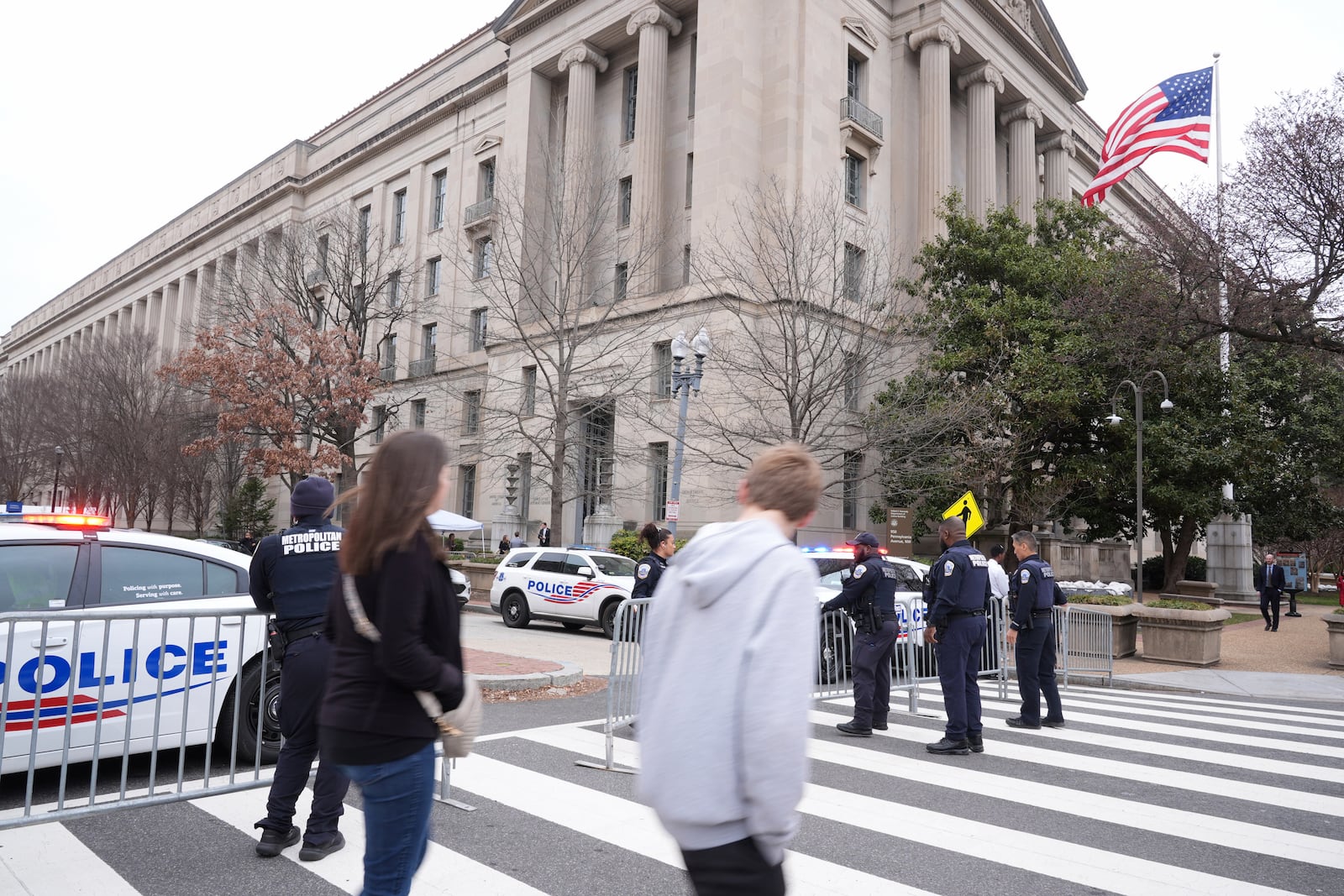 Pedestrians walk as police secure the area around the Justice Department before President Donald Trump speaks Friday, March 14, 2025, in Washington. (AP Photo/Jacquelyn Martin)