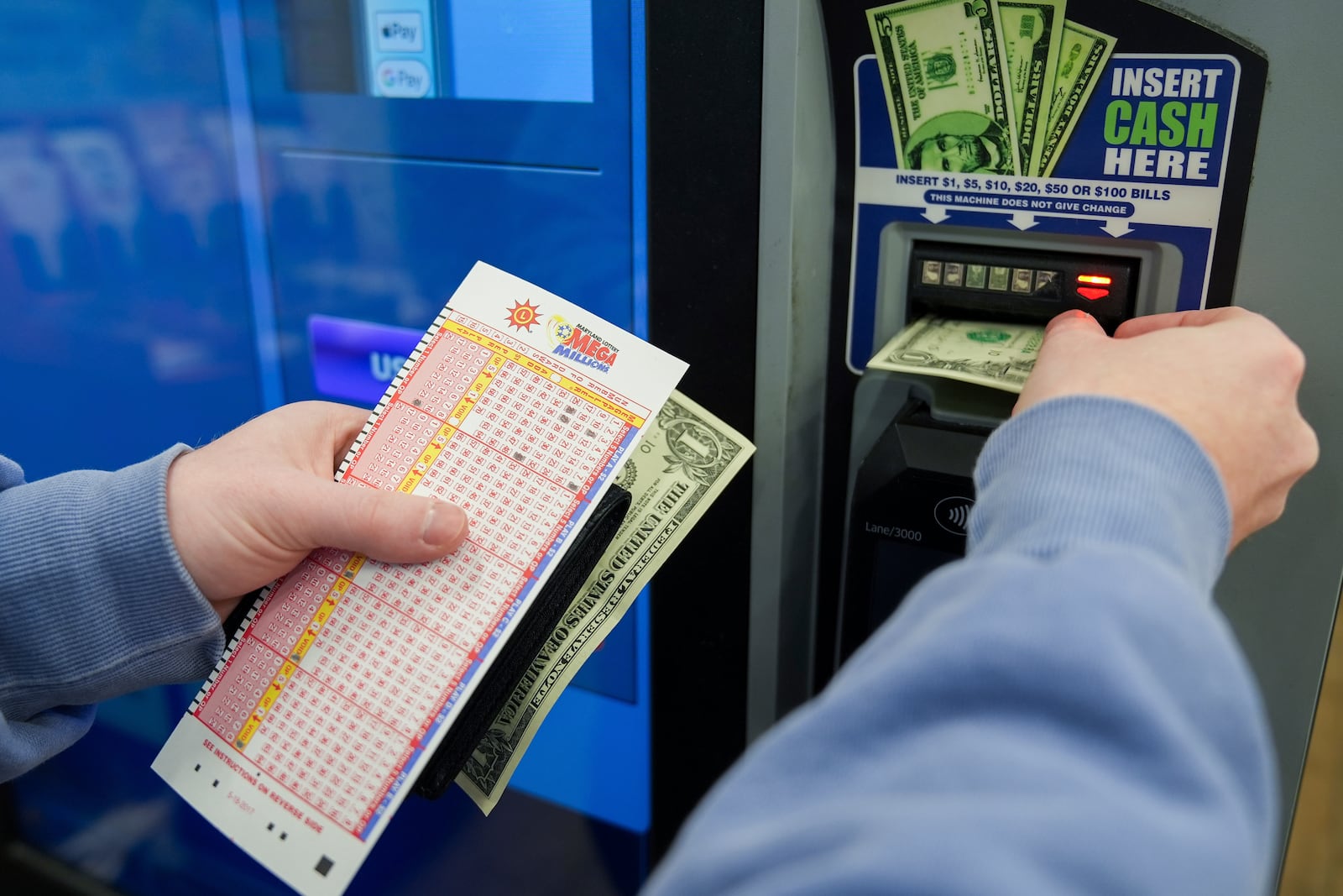 A person inserts cash into a self-serve terminal while holding their play slip ahead of Friday's Mega Millions drawing of $1.15 billion, Thursday, Dec. 26, 2024, in Baltimore. (AP Photo/Stephanie Scarbrough)