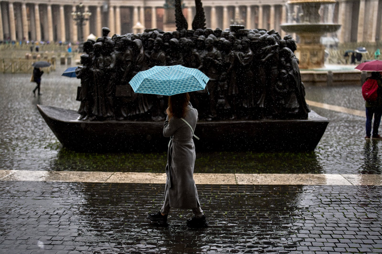 A woman looks at the "Angels Unawares" boat sculpture by Canadian artist Timothy P. Schmalz on a rainy day in St. Peter's square at The Vatican, Wednesday, March 12, 2025. (AP Photo/Francisco Seco)