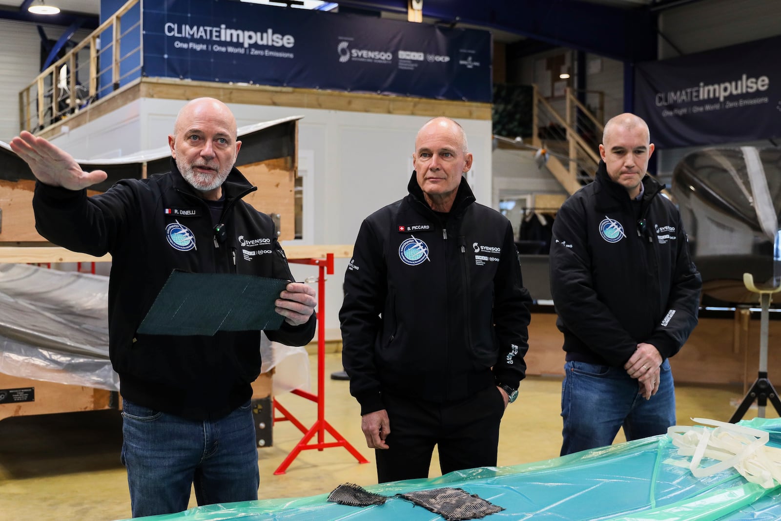 Swiss aviation pioneer Bertrand Piccard, center, Raphael Dinelli, left, Climate Impulse engineer and co-pilot, and project manager Cyril Haenel speak in front of the wings of the Climate Impulse, a plane powered by liquid hydrogen, at the press presentation of the project in a hangar in Les Sables d'Olonne, France on Thursday, Feb. 13, 2025.(AP Photo/Yohan Bonnet)