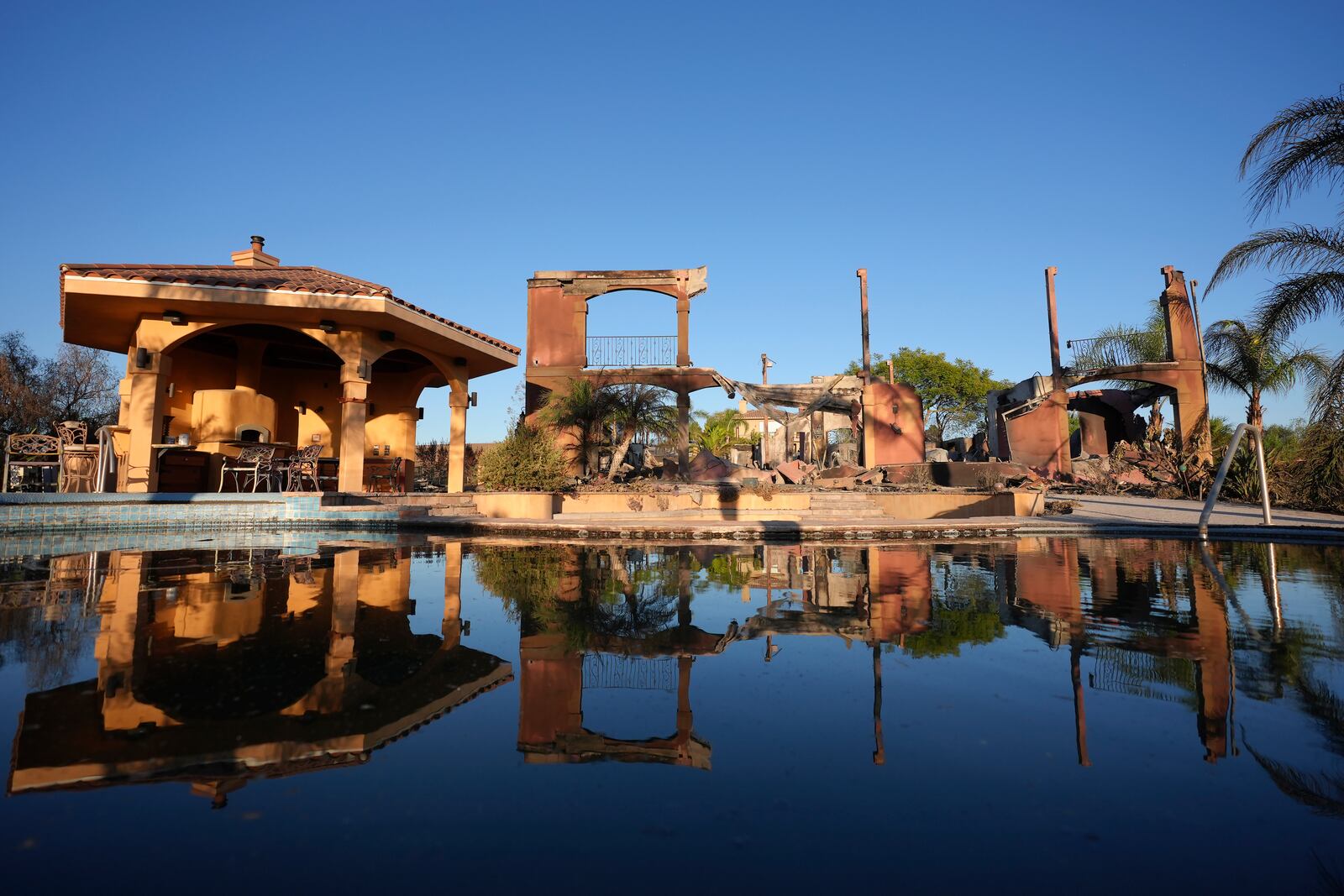 A home destroyed by the Mountain Fire is reflected in water from a swimming pool in Camarillo, Calif., Friday, Nov. 8, 2024. (AP Photo/Jae C. Hong)