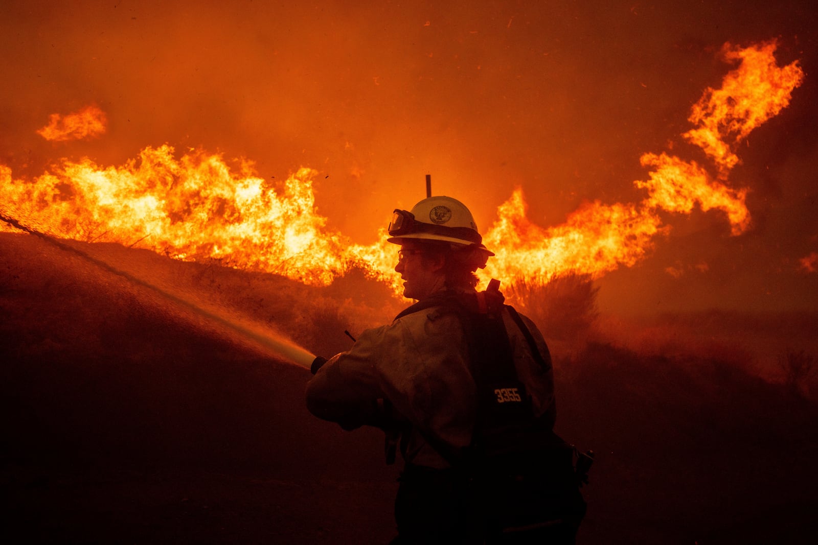 A firefighters spray water as he monitor flames caused by the Hughes Fire along a roadside in Castaic, Calf., Wednesday, Jan. 22, 2025. (AP Photo/Ethan Swope)