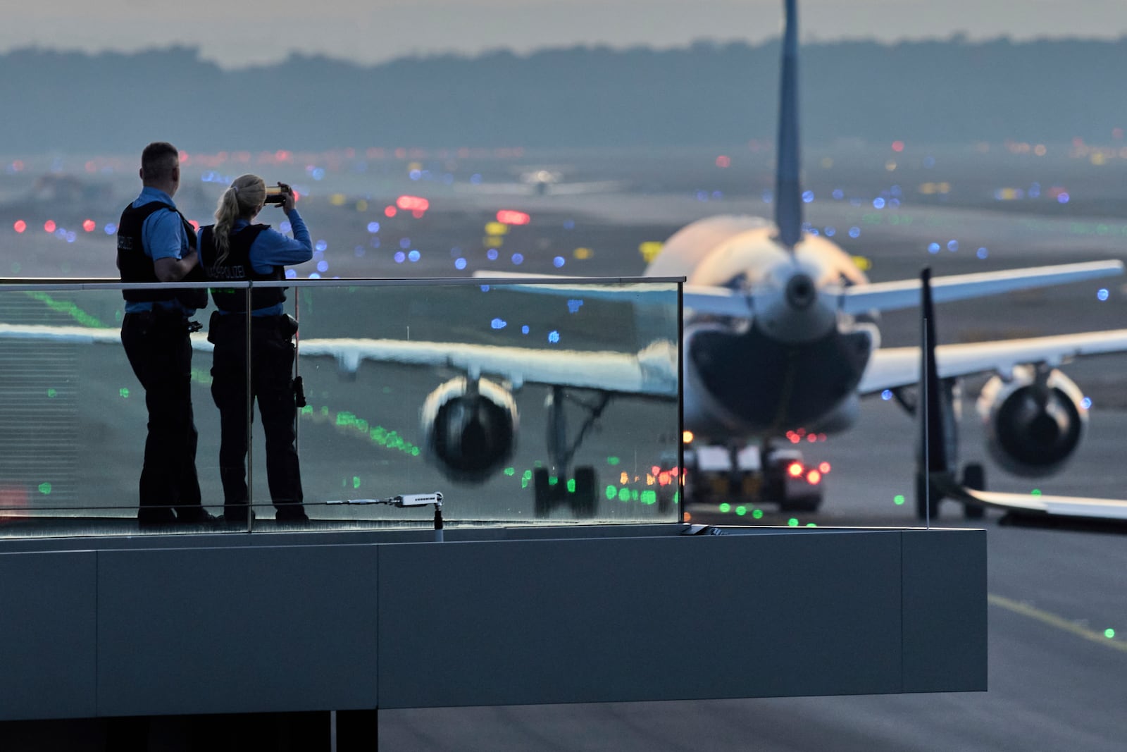 Police officers watch aircrafts take their parking positions at the airport in Frankfurt, Germany, Sunday, March 9, 2025, the evening before a warning strike of all major German airports. (AP Photo/Michael Probst)