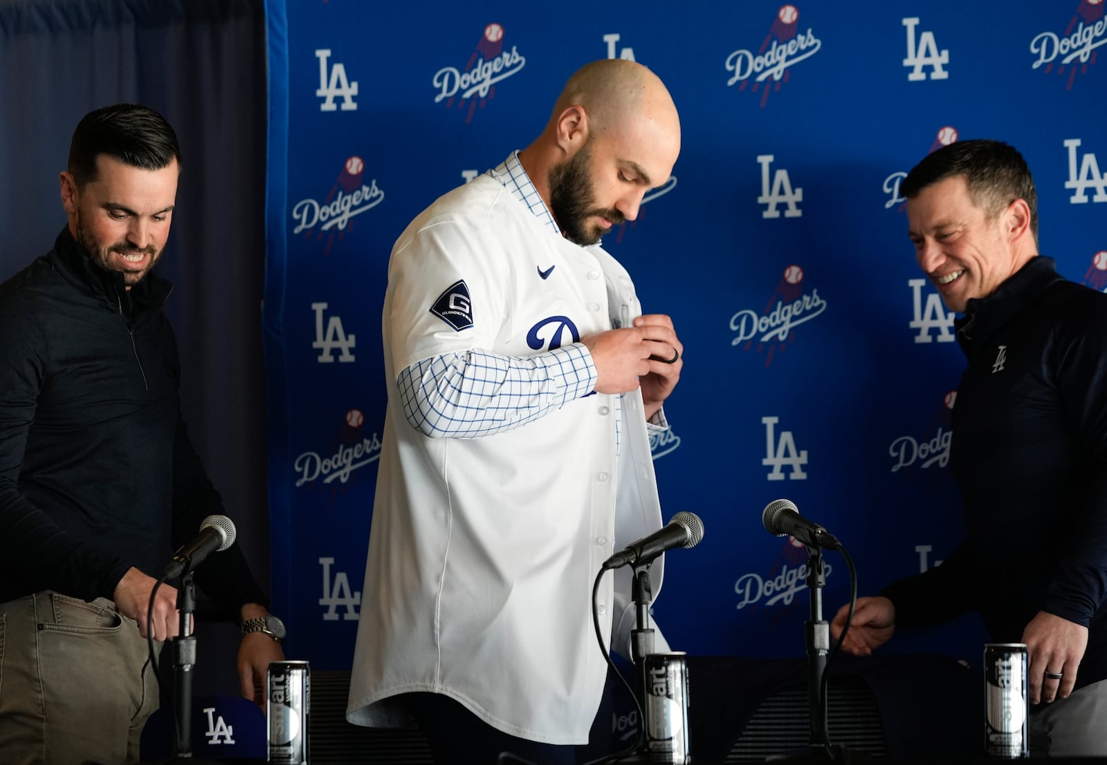 Andrew Friedman president of baseball operations for the Los Angeles Dodgers, right, and Executive Vice President and General Manager Brandan Gomes, left, watch as left-handed reliever Tanner Scott puts on a Dodgers jersey at an introduction news conference at Dodger Stadium in Los Angeles on Thursday, Jan. 23, 2025. (AP Photo/Richard Vogel)