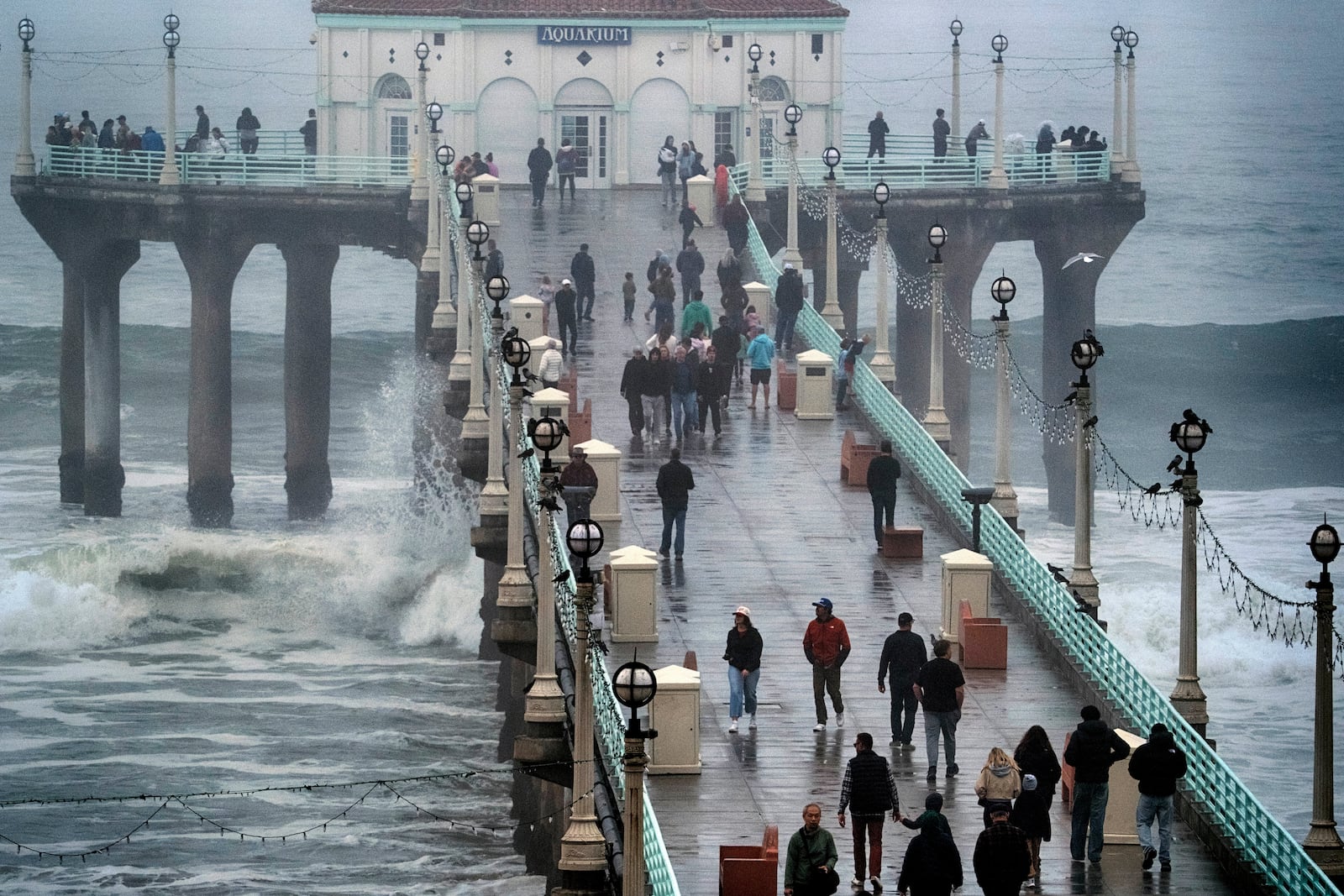 People brave the rain and walk along the Manhattan Beach Pier to watch high surf on Tuesday, Dec. 24, 2024 in Manhattan Beach, Calif. (AP Photo/Richard Vogel)