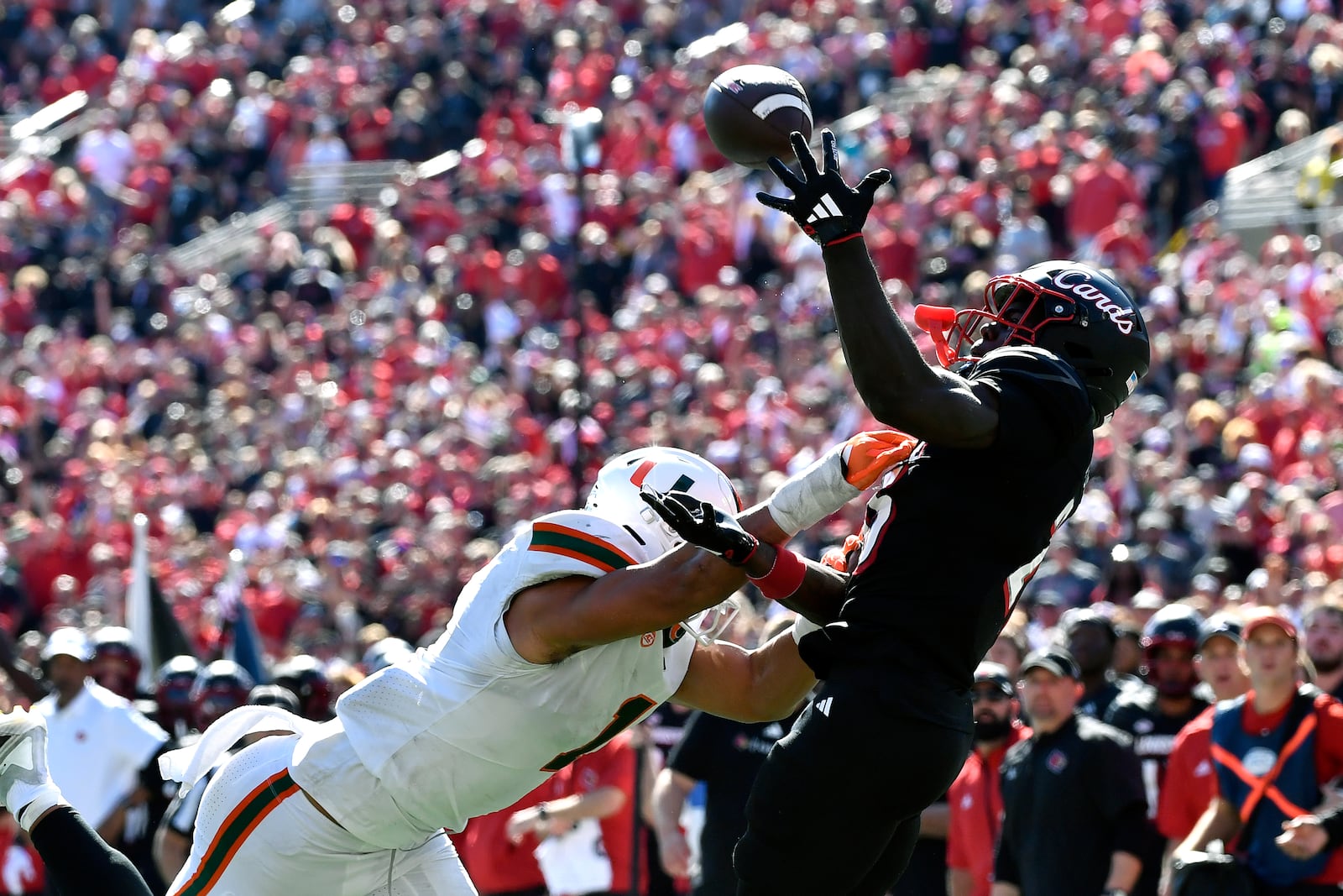 Louisville running back Isaac Brown (25) attempts to make a catch over the defense of Miami linebacker Francisco Mauigoa (1) during the second half of an NCAA college football game in Louisville, Ky., Saturday, Oct. 19, 2024. Miami won 52-45. (AP Photo/Timothy D. Easley)