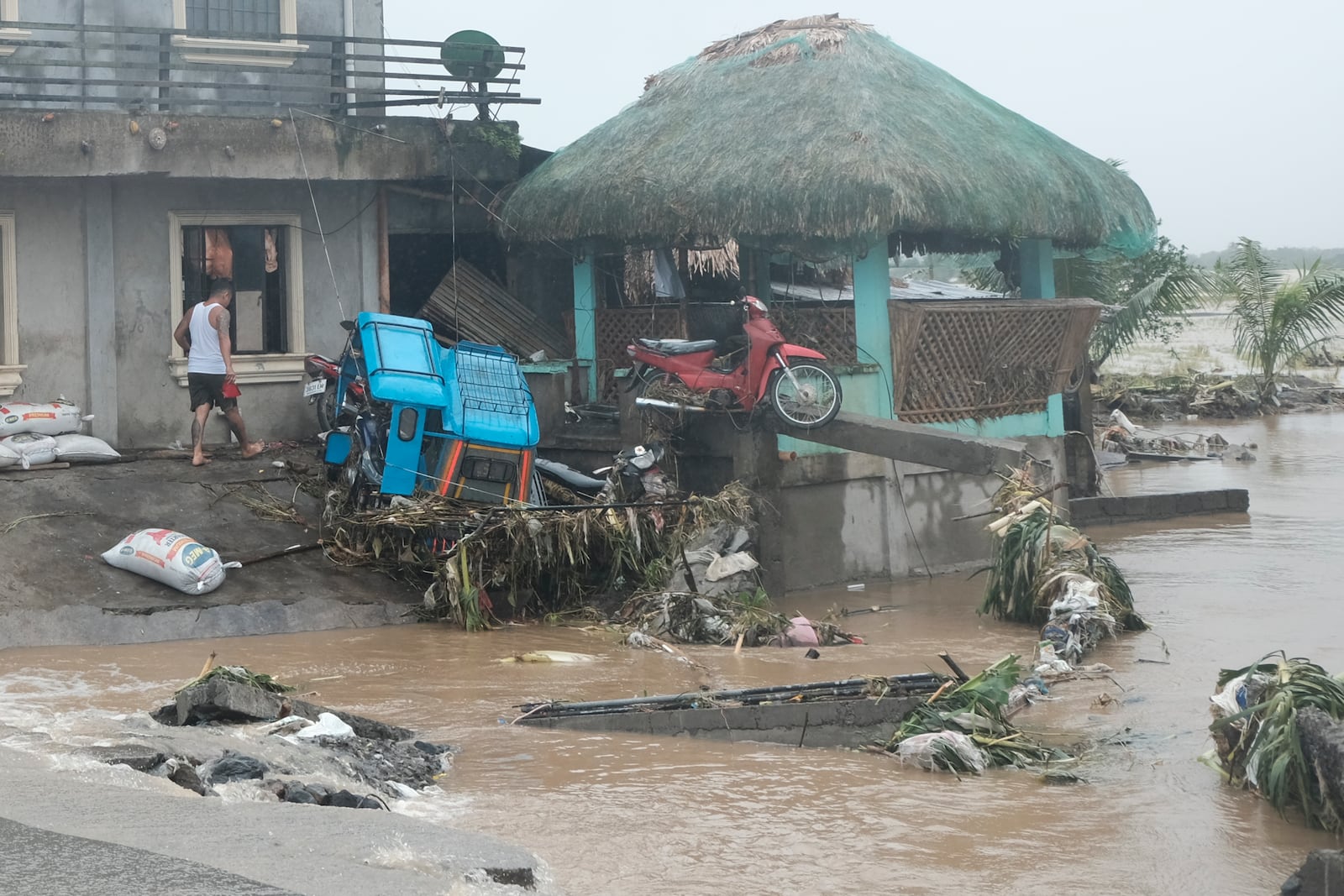 A man walks past damages caused by flash floods on Thursday Oct. 24, 2024 after Tropical Storm Trami, locally named Kristine, dumped heavy rains at Libon town, Albay province, Philippines. (AP Photo/John Michael Magdasoc)