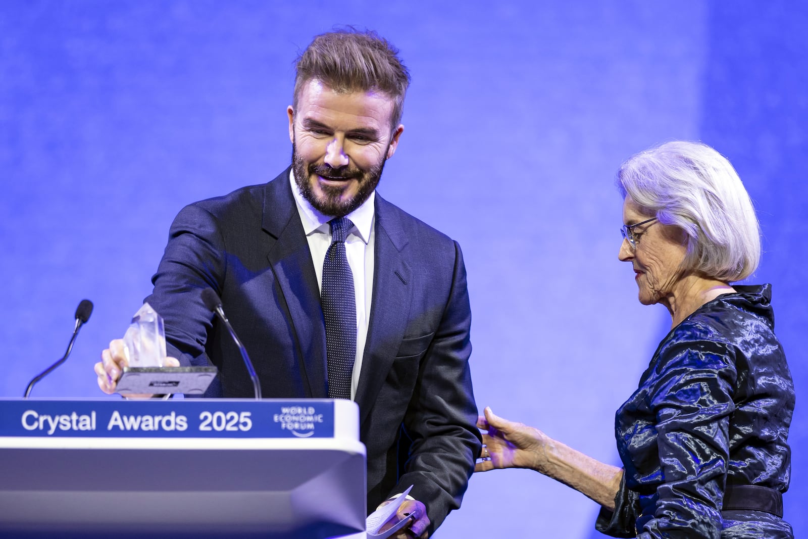 David Beckham prepares to speak after receives a Crystal Award from Hilde Schwab, Chairperson and Co-Founder, Schwab Foundation for Social Entrepreneurship, right, during the ceremony for the Crystal Awards at the 55th annual meeting of the World Economic Forum, WEF, in Davos, Switzerland, on Monday, Jan. 20, 2025. (Michael Buholzer/Keystone via AP)