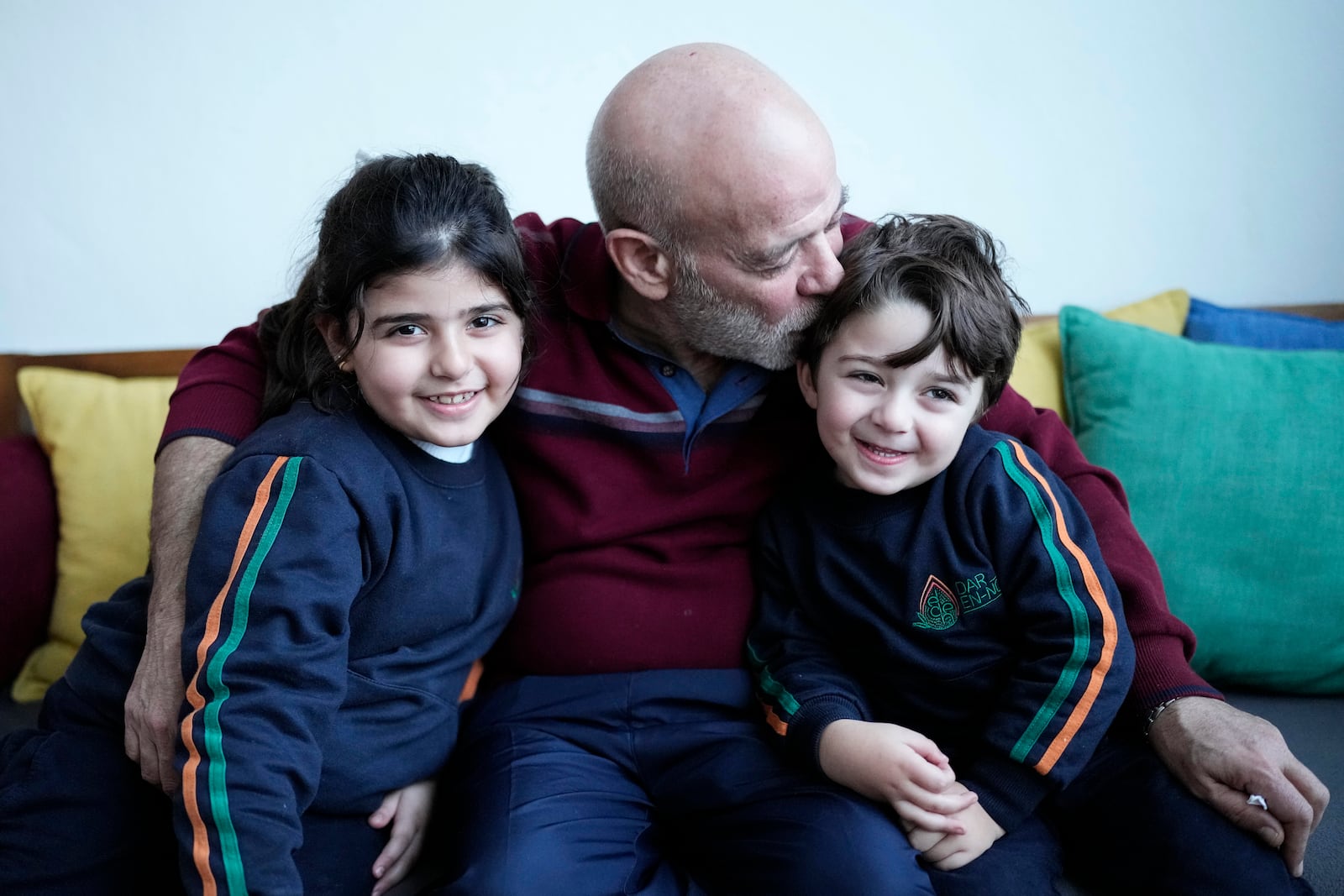 Suheil Hamwi, center, who spent 32 years in prison in Syria and returned to Lebanon after the government of Bashar Assad was toppled kisses his grandchildren at his home in Chekka, Lebanon, Tuesday, Dec. 10, 2024. (AP Photo/Hassan Ammar)