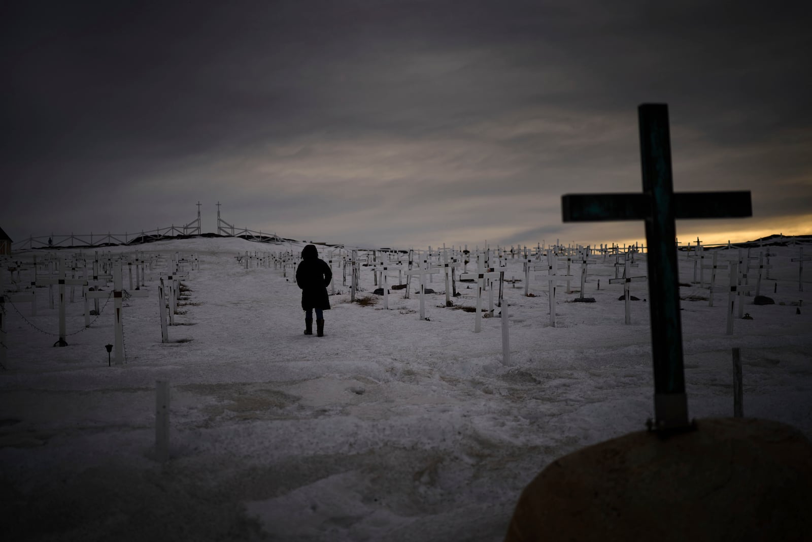 A woman walks at a graveyard covered by snow as the sun sets in Nuuk, Greenland, Sunday, Feb. 16, 2025. (AP Photo/Emilio Morenatti)