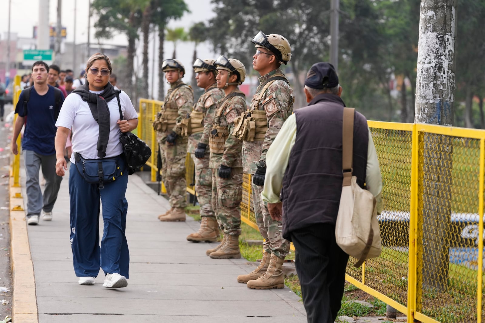 Pedestrians walk past soldiers guarding a bridge in Lima, Peru, Tuesday, March 18, 2025, after President Dina Boluarte declared a state of emergency following the killing of a popular singer amid a surge in violence in the capital. (AP Photo/Martin Mejia)