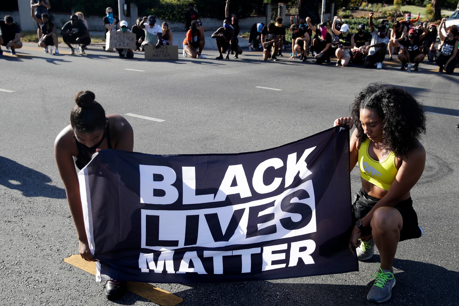 FILE - Alycia Pascual-Pena, left, and Marley Ralph kneel while holding a Black Lives Matter banner during a protest in memory of Breonna Taylor, in Los Angeles, July 11, 2020. (AP Photo/Marcio Jose Sanchez, File)