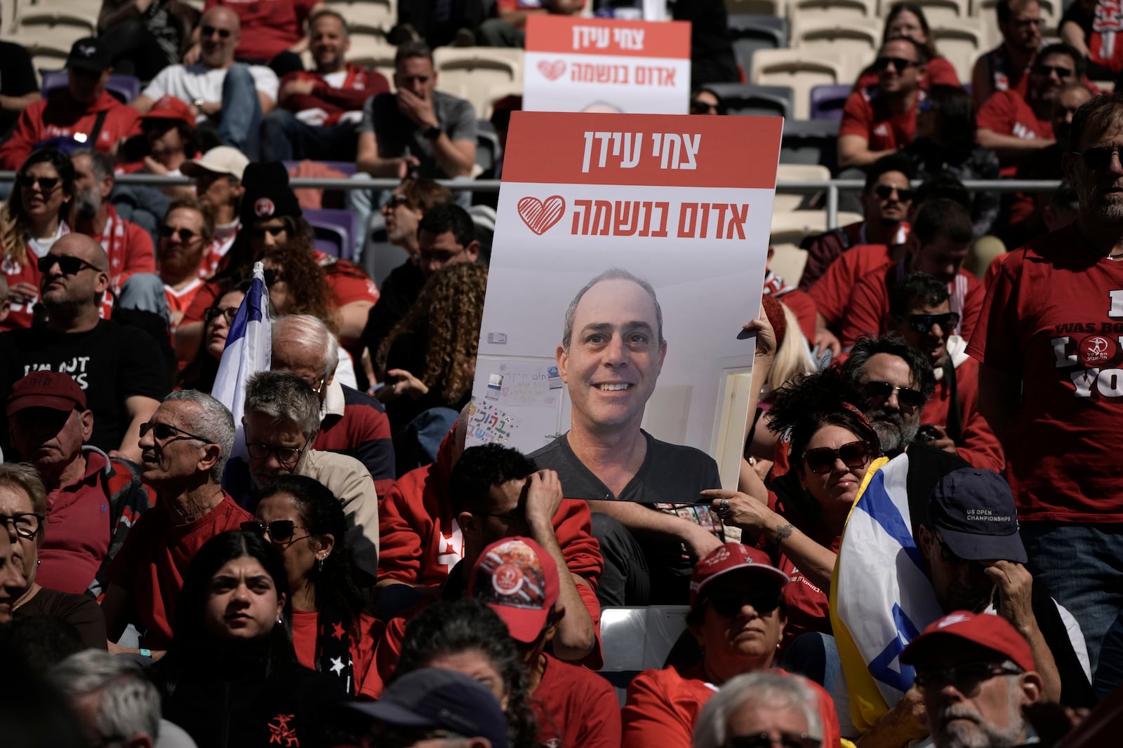 People attend a public memorial ceremony for slain hostage Tsachi Idan, a fan of Hapoel Tel Aviv F.C., who was killed in Hamas captivity in the Gaza Strip, at Bloomfield Stadium in Tel Aviv, Israel, Friday, Feb. 28, 2025. Hebrew: "Tsachi Idan - red in the soul." (AP Photo/Leo Correa)