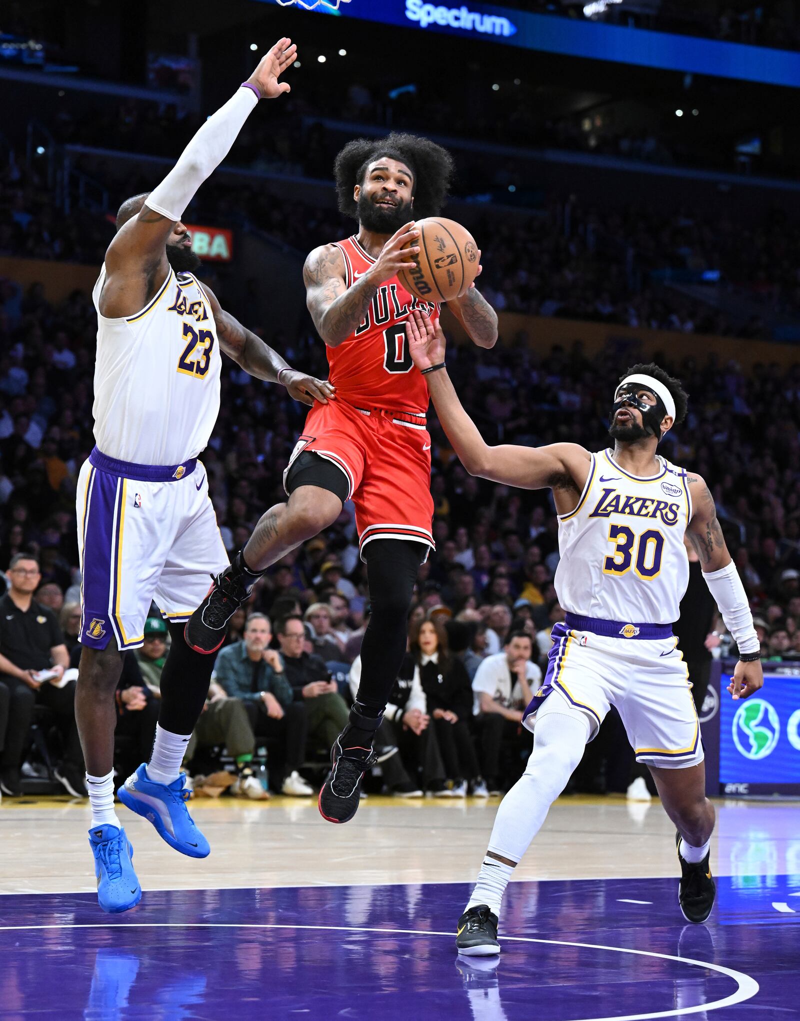 Chicago Bulls guard Coby White (0) drives between Los Angeles Lakers forward LeBron James (23) and guard Jordan Goodwin (30) for a basket in the first half of an NBA basketball game Saturday, March 22, 2025, in Los Angeles. (AP Photo/Wally Skalij)