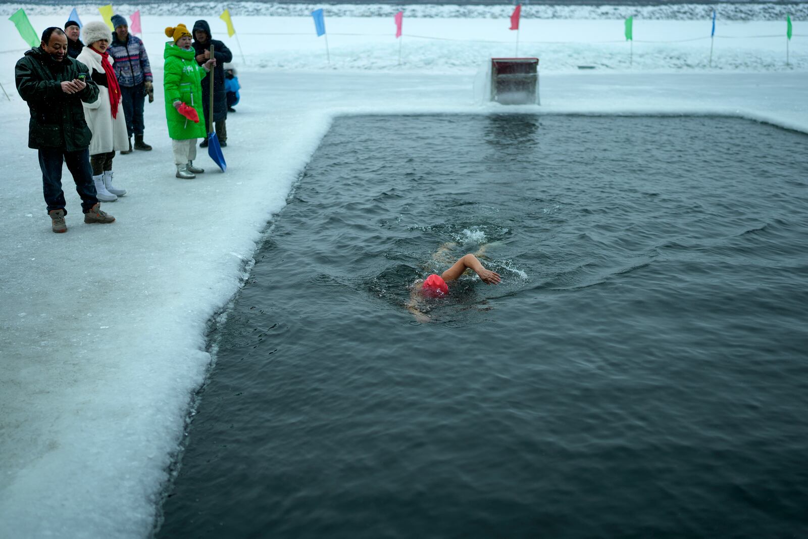 Residents watch a woman swim in a pool carved from ice on the frozen Songhua river in Harbin in northeastern China's Heilongjiang province, Tuesday, Jan. 7, 2025. (AP Photo/Andy Wong)