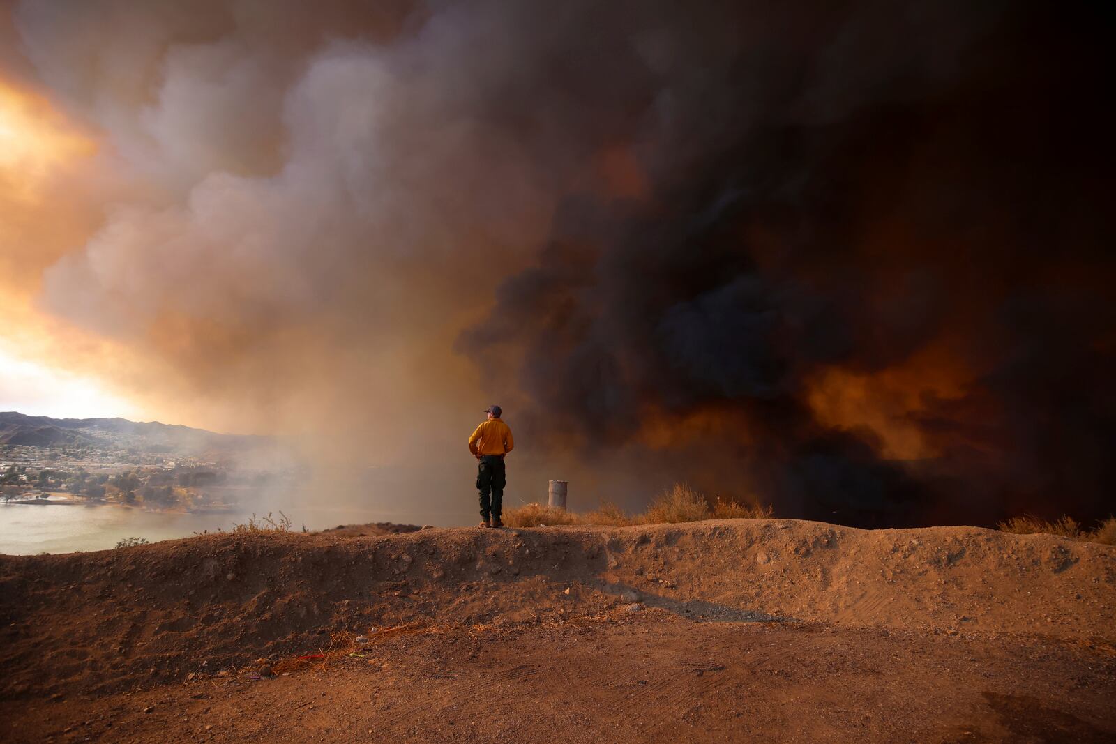 A firefighter looking out towards Lake Castaic stands on a mound backdropped by clouds of smoke caused by the Hughes Fire in Castaic, Calf., Wednesday, Jan. 22, 2025. (AP Photo/Ethan Swope)