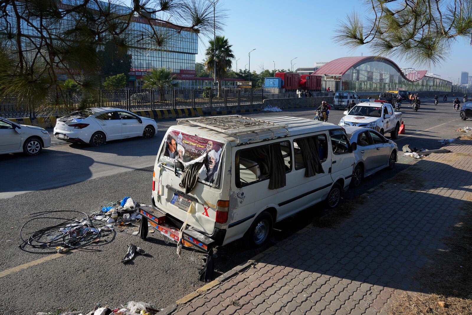 A motorcyclist drives through the damaged vehicles left behind by supporters of imprisoned former Prime Minister Imran Khan's Pakistan Tehreek-e-Insaf party when security forces launched an operation Tuesday night to disperse them, in Islamabad, Pakistan, Wednesday, Nov. 27, 2024. (AP Photo/Anjum Naveed)