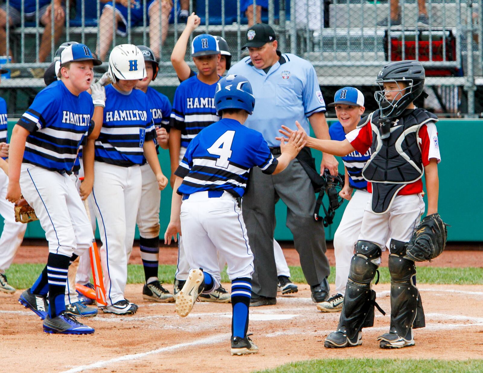 Hamilton West Side’s Davis Avery (4) is greeted by his teammates — and Wausau National (Wis.) catcher Roger Stroming (22) — after hitting a home run during their Little League Great Lakes Regional game Sunday at the Grand Park Sports Campus in Westfield, Ind. GREG LYNCH/STAFF