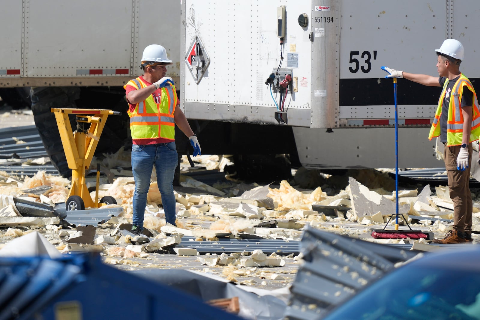 Workers talk while cleaning up debris from a damaged warehouse after storms moved through Tuesday, March 4, 2025, in Lewisville, Texas. (AP Photo/LM Otero)