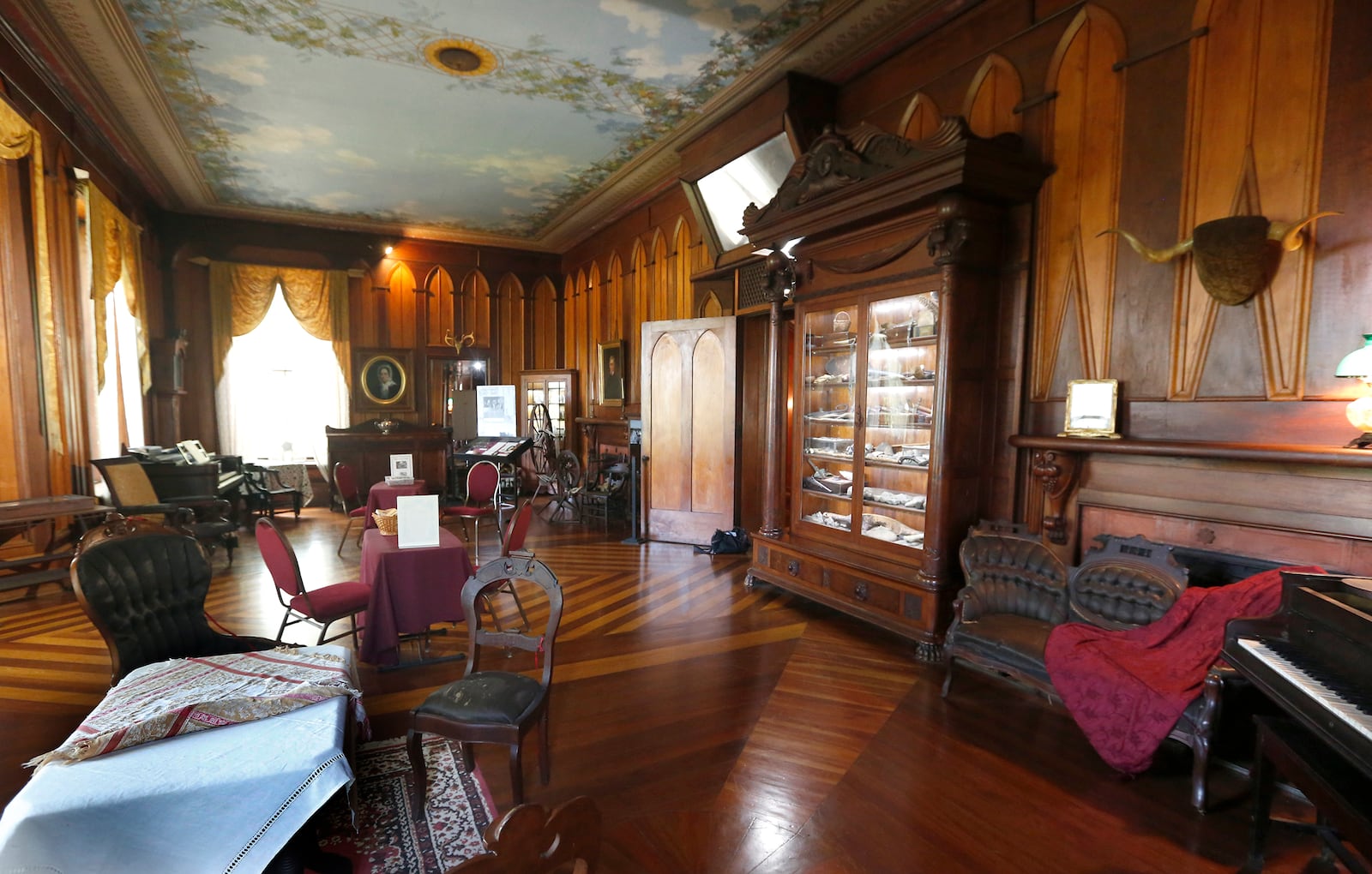 Margaret Piatt calls the drawing room at Mac-A-Cheek âthe best room with the best things in it.â It was the original portion of the home that opened as a museum in 1912. A massive cabinet filled with natural history treasures collected by William McCoy Piatt is at right. LISA POWELL / STAFF