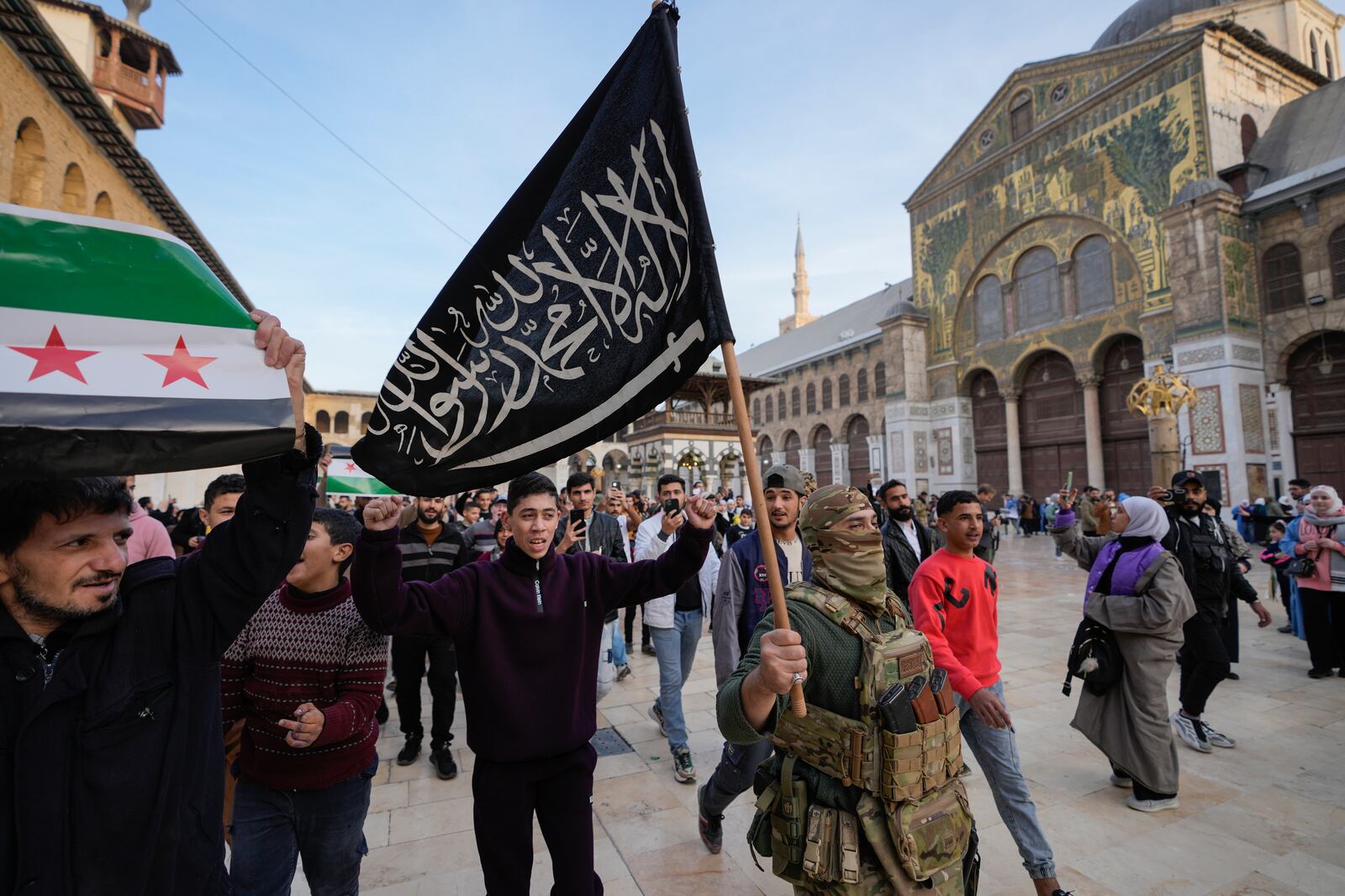 A masked opposition fighter carries a flag of Hayat Tahrir al-Sham (HTS) in the courtyard of the Umayyad Mosque in the old walled city of Damascus, Syria, on Tuesday, Dec. 10, 2024. HTS is the largest rebel faction within the opposition that toppled Bashar Assad's regime last Sunday. (AP Photo/Hussein Malla)