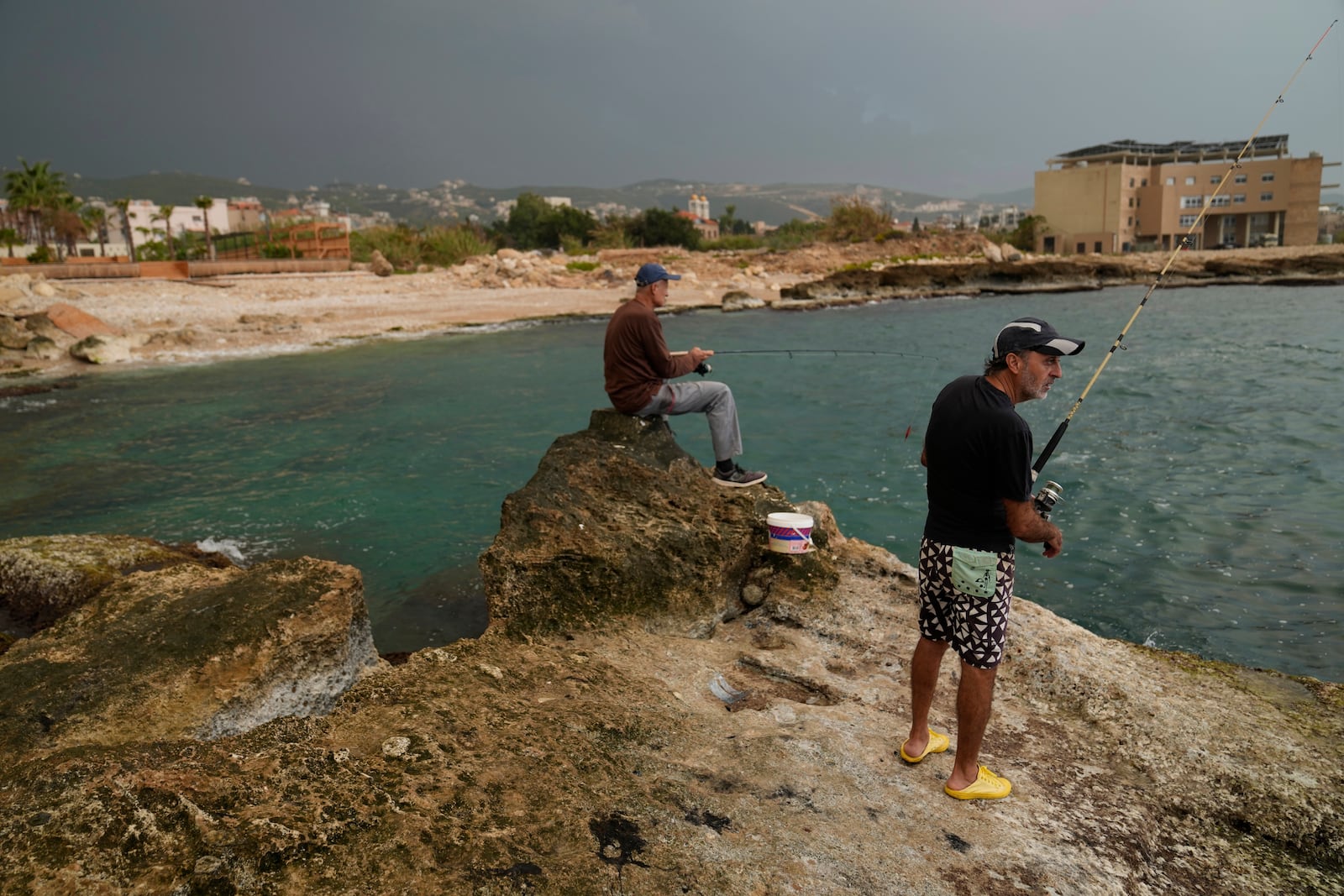 Lebanese fishermen cast their fishing rods at a beach in Batroun, northern Lebanon, Saturday, Nov. 2, 2024, where Lebanese officials say a ship captain was taken away by a group of armed men who landed on a coast north of Beirut and they're investigating whether Israel was involved. (AP Photo/Hussein Malla)