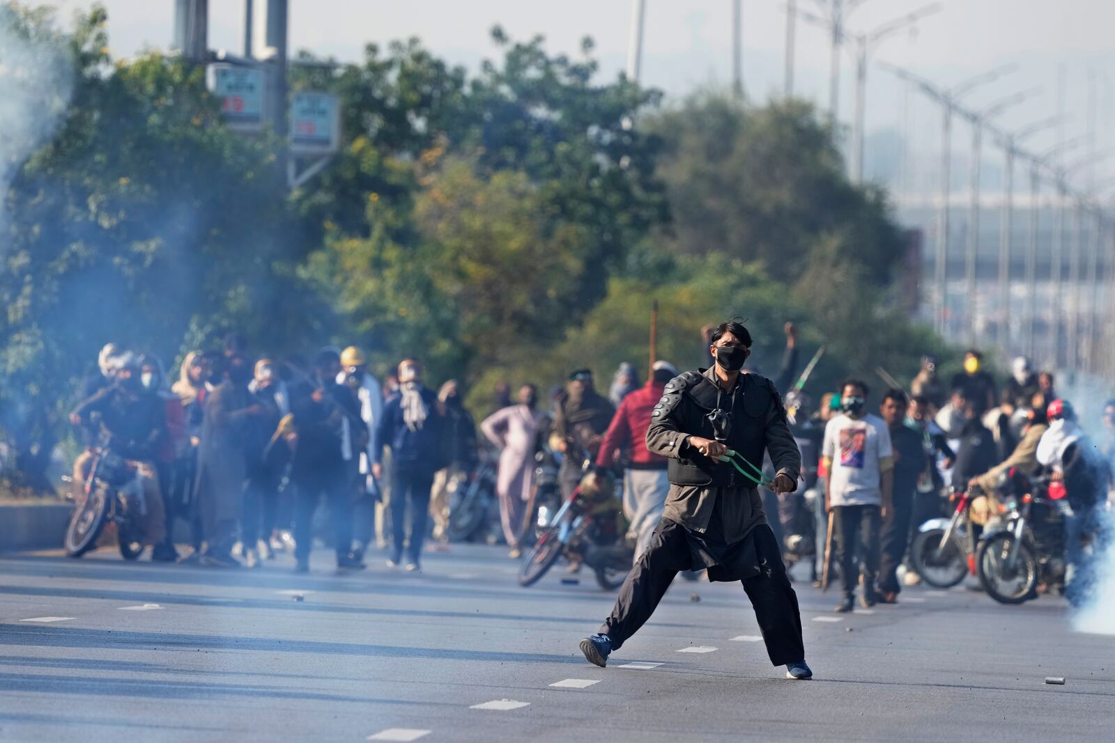 Supporters of imprisoned former premier Imran Khan's Pakistan Tehreek-e-Insaf party, aim to throw stones with slingshot following police fire tear gas shell to disperse them during clashes, in Islamabad, Pakistan, Tuesday, Nov. 26, 2024. (AP Photo/Anjum Naveed)