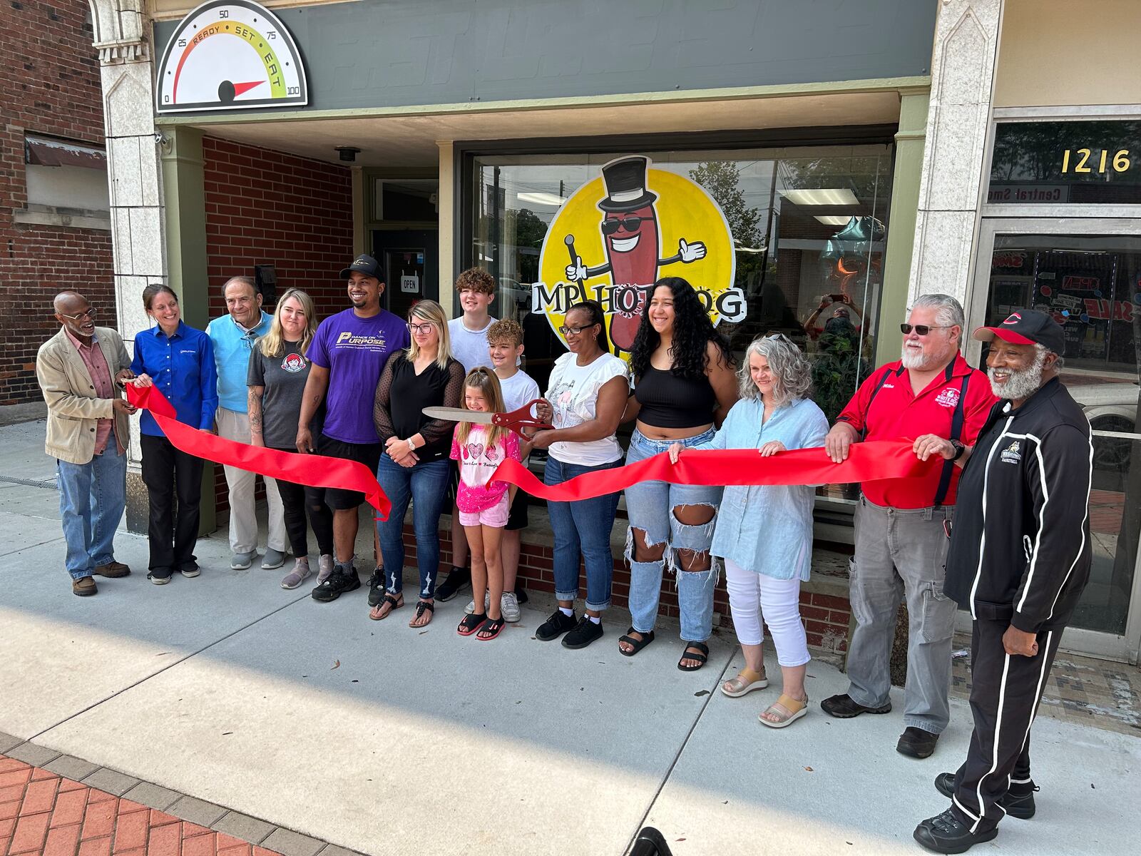 Rachelle Edwards, owner of Mr. Hot Dog on Central Avenue in Middletown, cuts the ribbon during a ceremony Tuesday morning. She was joined by Downtown Middletown Inc. representatives and family and friends. RICK McCRABB/STAFF