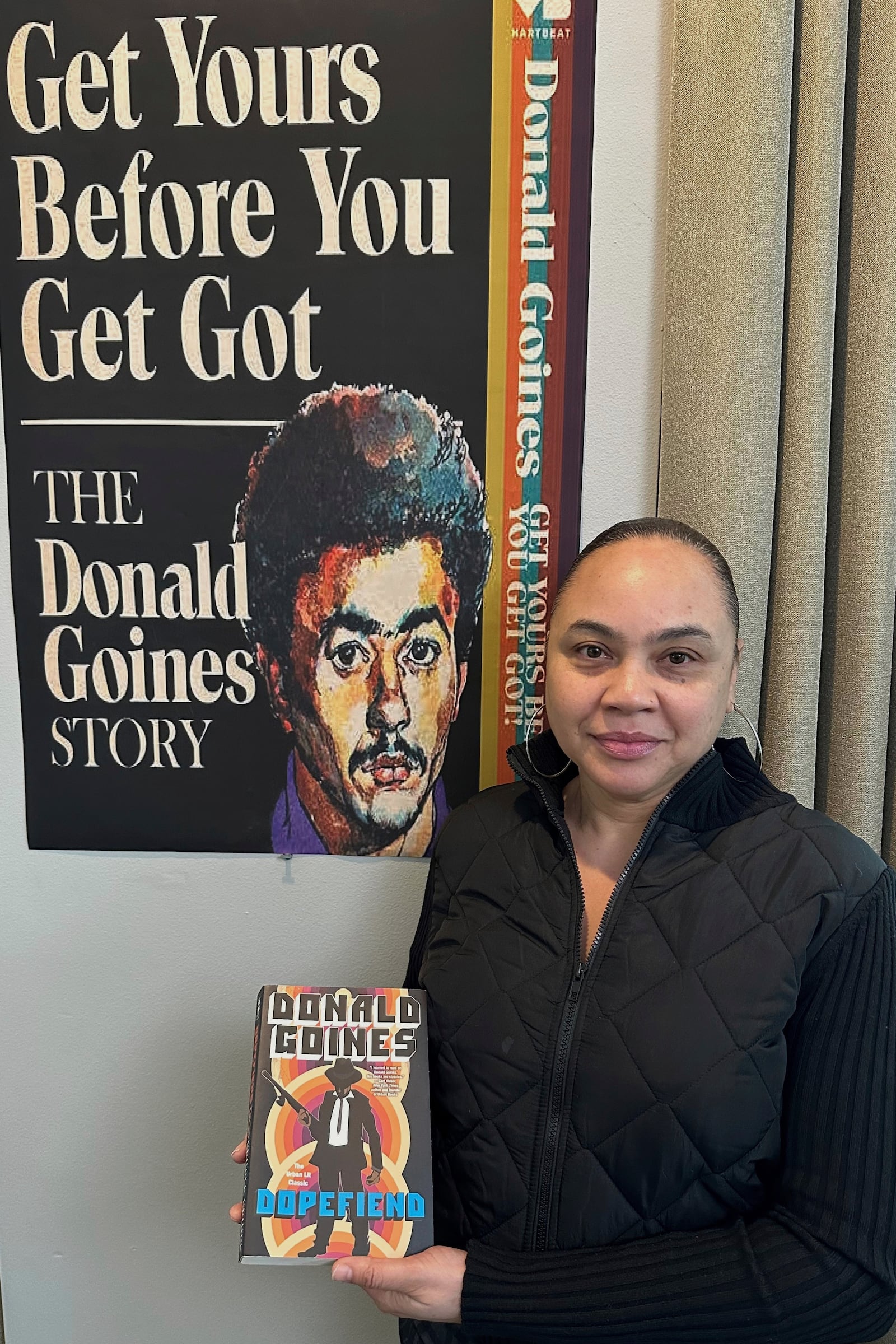 Donna Sailor poses next to poster of upcoming documentary about the life of her father and urban literature writer Donald Goines on Wednesday, March 12, 2025 in Detroit. (AP Photo/Corey Williams)