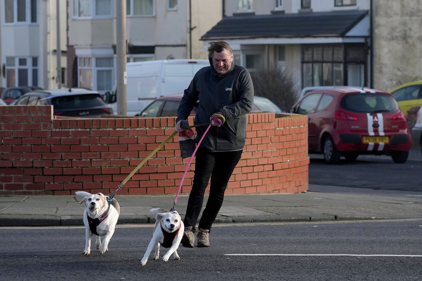 A man walking two dogs braves the wind as Storm Eowyn hits the country in Blackpool, England, Friday, Jan. 24, 2025.(AP Photo/Jon Super)