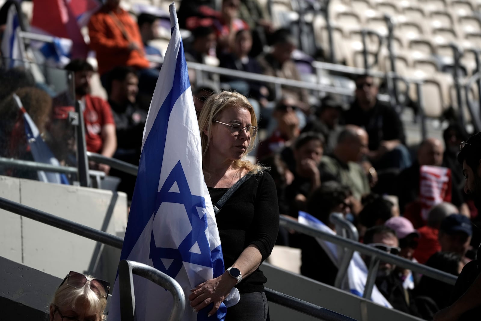 A mourner holds the Israeli flag at a public memorial ceremony for slain hostage Tsachi Idan, a fan of Hapoel Tel Aviv F.C., who was killed in Hamas captivity in the Gaza Strip, at Bloomfield Stadium in Tel Aviv, Israel, Friday, Feb. 28, 2025. (AP Photo/Leo Correa)