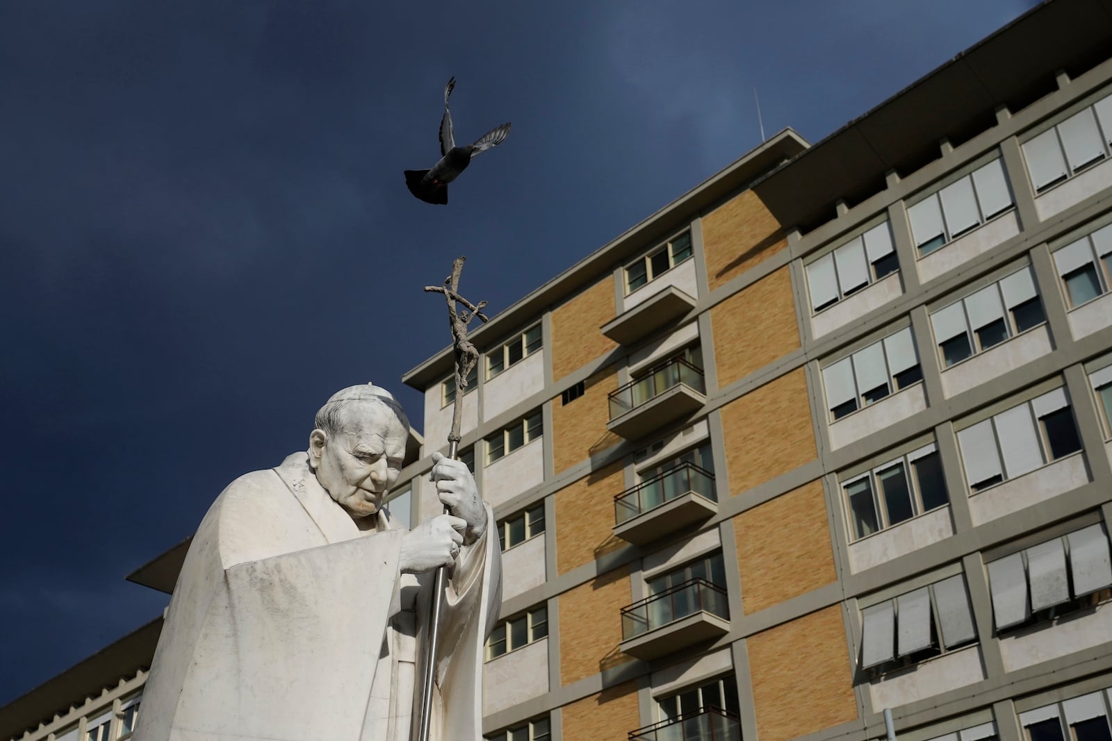 A marble statue of late Pope John Paul II is backdropped by the Agostino Gemelli Polyclinic in Rome, Saturday, Feb. 15, 2025, where Pope Francis was hospitalised Friday after a weeklong bout of bronchitis worsened and is receiving drug therapy for a respiratory tract infection. (AP Photo/Alessandra Tarantino)