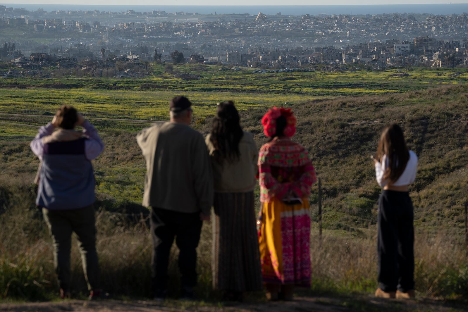 People look at buildings that were destroyed during the Israeli air and ground offensive stand in the Gaza Strip as seen from southern Israel, Sunday, March 2, 2025. (AP Photo/Leo Correa)