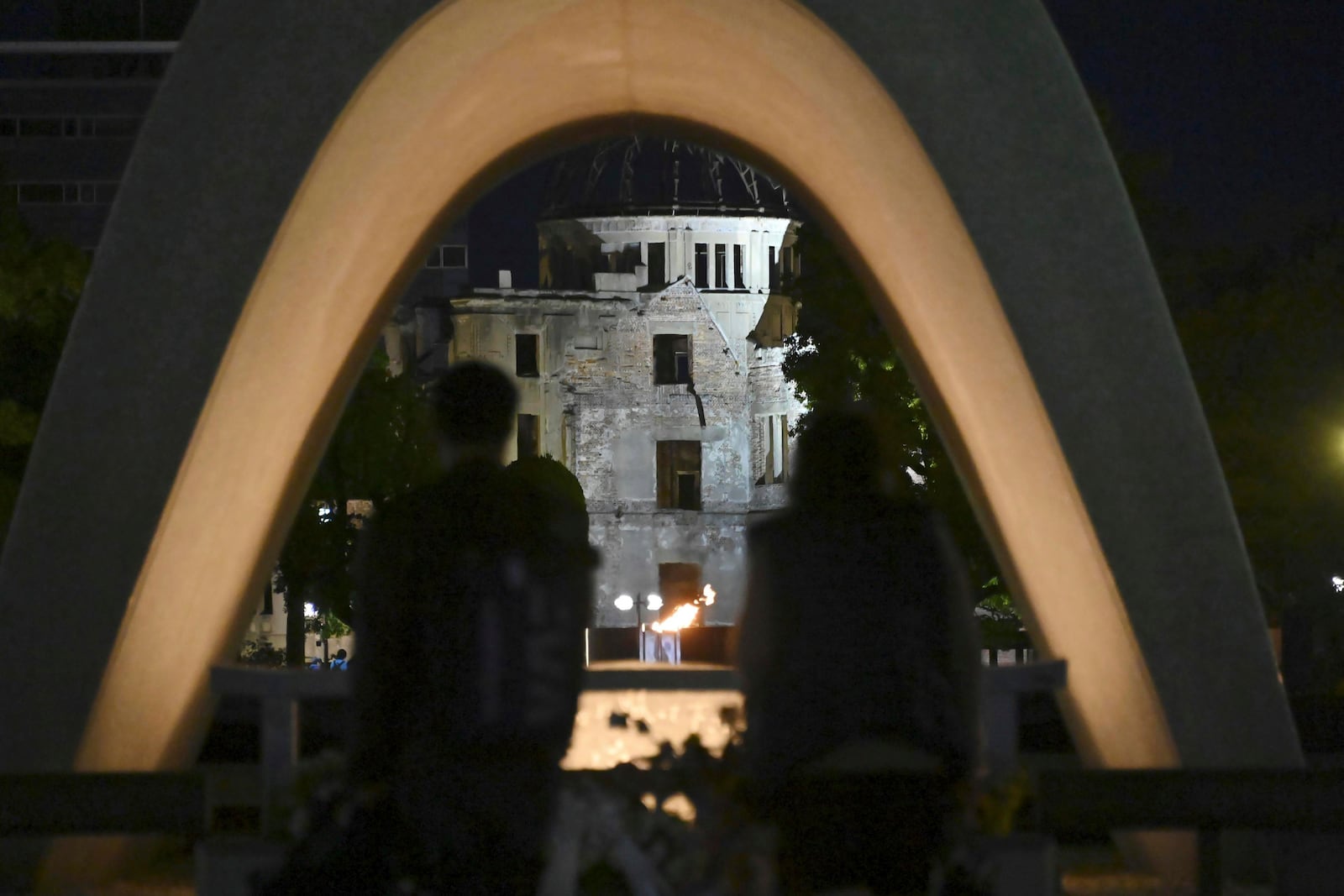 Visitors stand in front of the cenotaph for Atomic Bomb Victims at the Peace Memorial Park with the Atomic Bomb Dome seen in the background in Hiroshima, western Japan Friday, Oct. 11, 2024, after the Nobel Peace Prize was awarded to Nihon Hidankyo, a Japanese organization of survivors of the U.S. atomic bombings of Hiroshima and Nagasaki, for its activism against nuclear weapons. (Kyodo News via AP)