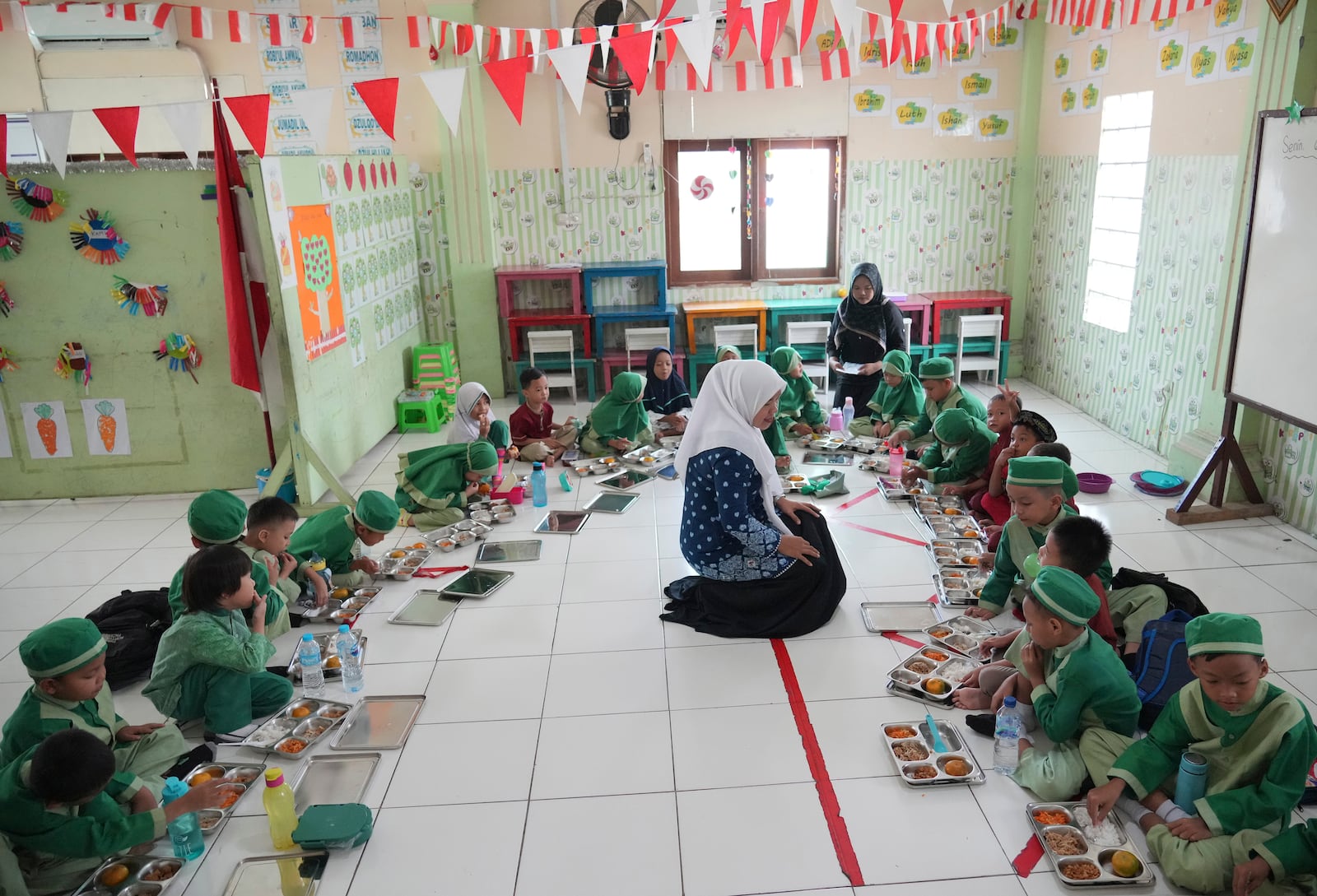 Students sit on the floor as they have their meals during the kick off of President Prabowo Subianto's ambitious free meal program to feed children and pregnant women nationwide despite critics saying that its required logistics could hurt Indonesia's state finances and economy at Early Childhood Education and Development in Jakarta, Indonesia, Monday, Jan. 6, 2025. (AP Photo/Achmad Ibrahim)