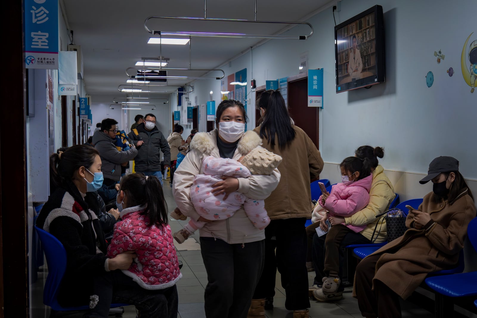 A woman wearing a face mask carries a child in her arms as she walks through a corridor crowded with patients at a pediatric hospital in southwest China's Chongqing Municipality on Jan. 7, 2025. (Chinatopix via AP)