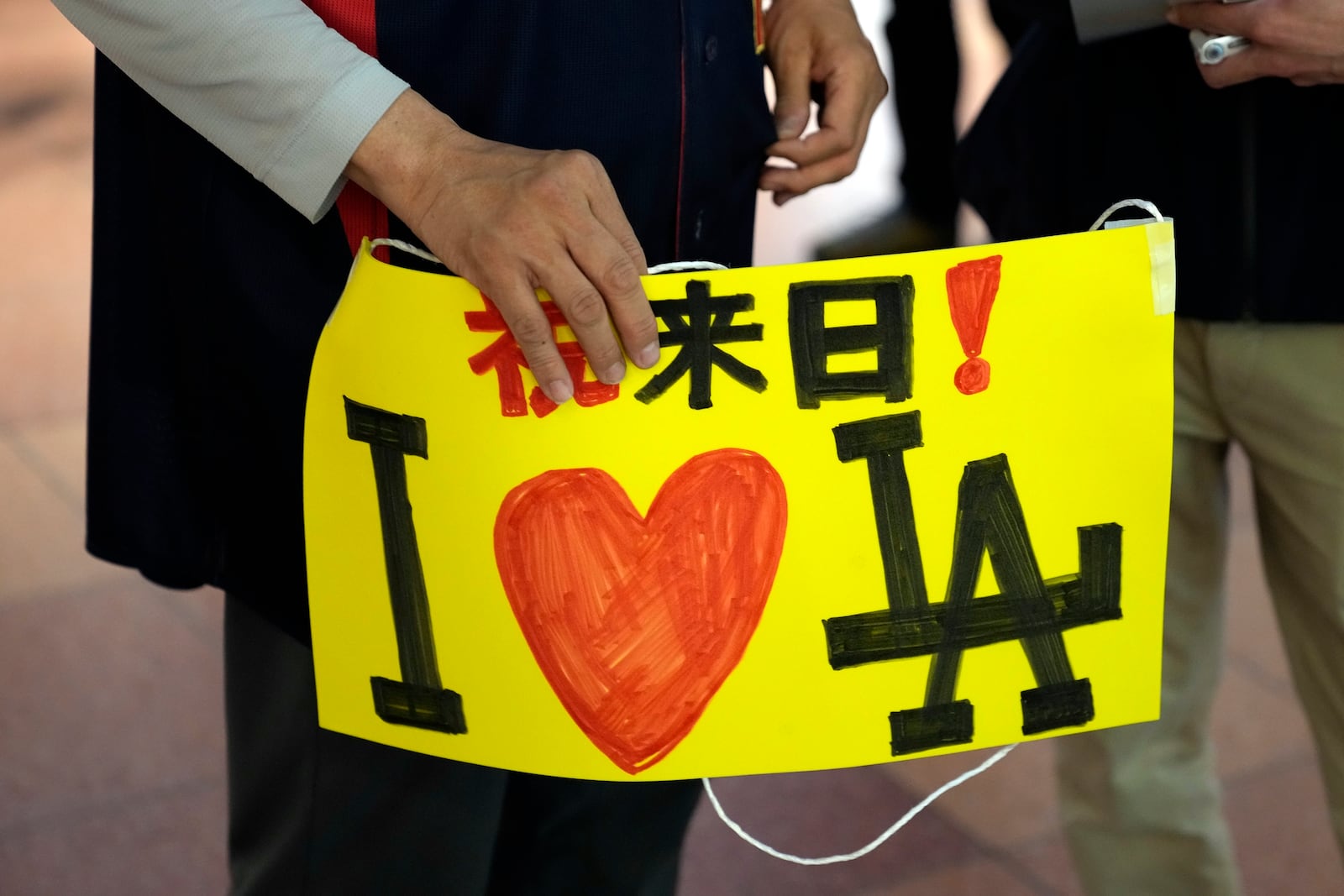 One of fans of Los Angeles Dodgers holds a banner says "Welcome to Japan! I love LA"as she waits for the team arrival at Tokyo International Airport Thursday, March 13, 2025, in Tokyo, as Los Angeles Dodgers is scheduled to play their MLB opening games against Chicago Cubs in Tokyo on March 18-19. (AP Photo/Hiro Komae)