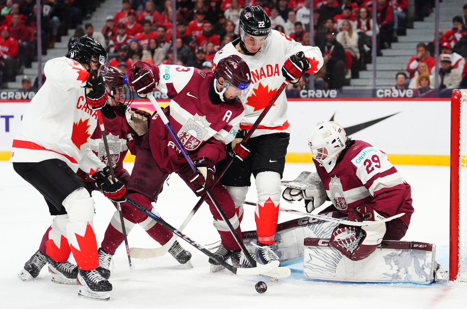 Canada's Berkly Catton, left, and Porter Martone (22) battle for the puck with Latvia's Viktors Kurbaka (3) in front of Latvia goaltender Linards Feldbergs (29) during second-period IIHF World Junior Hockey Championship preliminary round game action in Ottawa, Ontario, Friday, Dec. 27, 2024. (Sean Kilpatrick/The Canadian Press via AP)