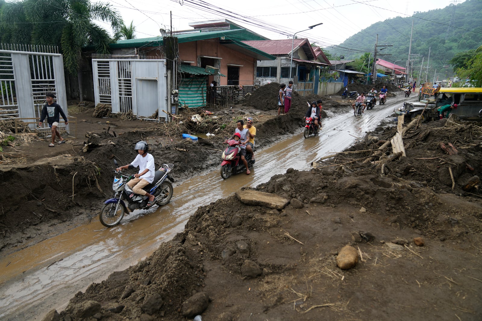 Residents ride motorcycles along a mud covered road after a landslide triggered by Tropical Storm Trami, recently struck Talisay, Batangas province, Philippines, Saturday, Oct. 26, 2024 . (AP Photo/Aaron Favila)