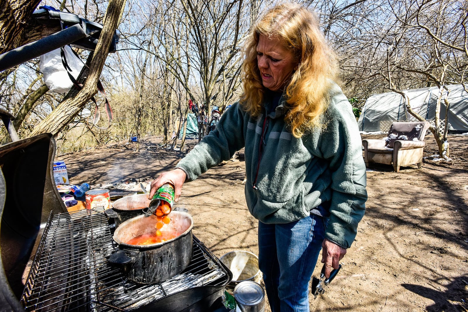 Lillie Nelson cooks soup on a propane grill at a homeless camp behind Hamilton Plaza shopping center Thursday, March 22. Nelson has lived in the camp for nearly a year. NICK GRAHAM/STAFF