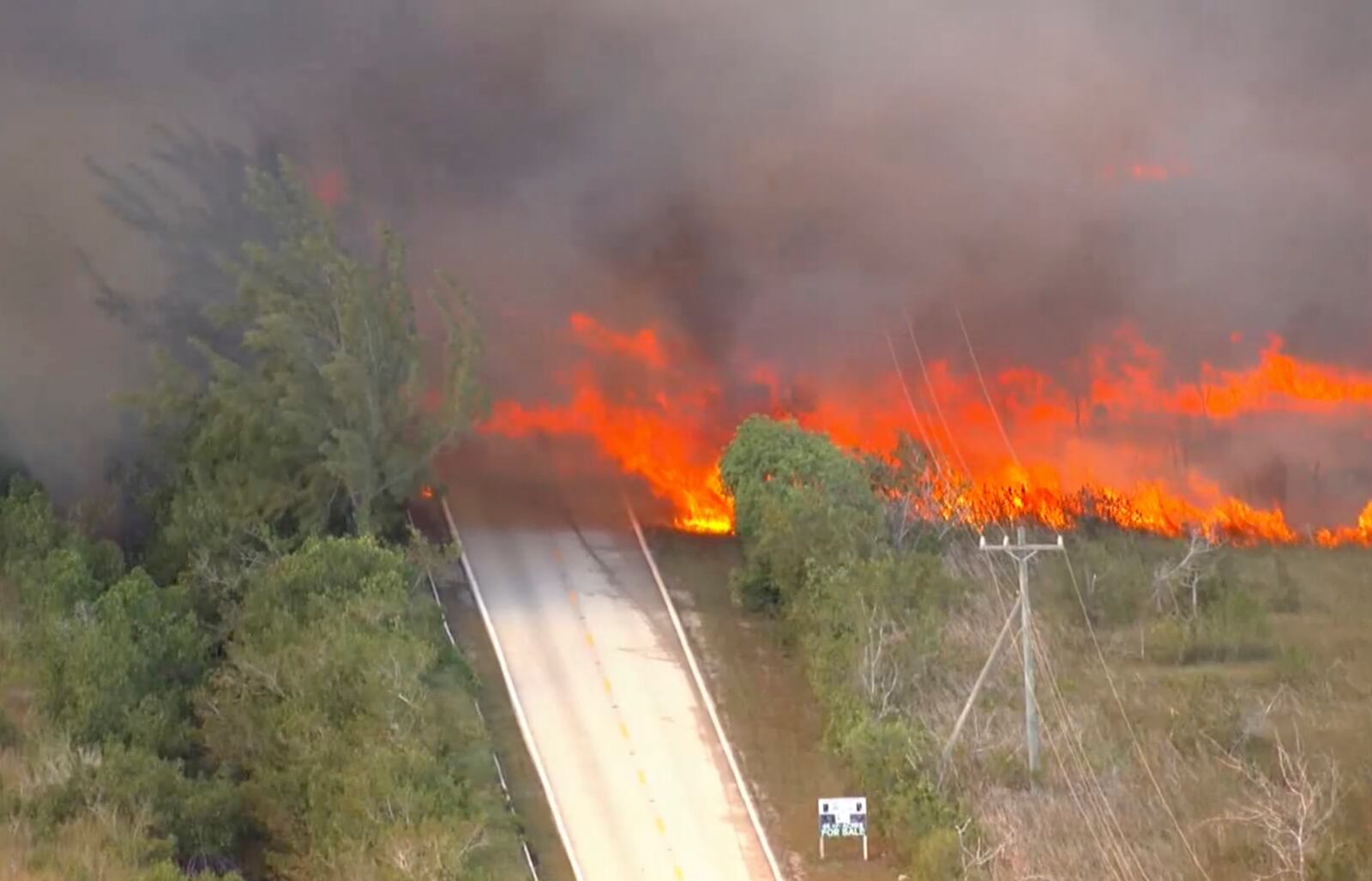 In this image taken from video provided by WSVN-TV, a brush fire burns across and over Card Sound Road, the only other road connecting the Keys to Florida City on the mainland, as it remains closed Tuesday, March 18, 2025, south of Dade County, Fla. (WSVN-TV via AP)