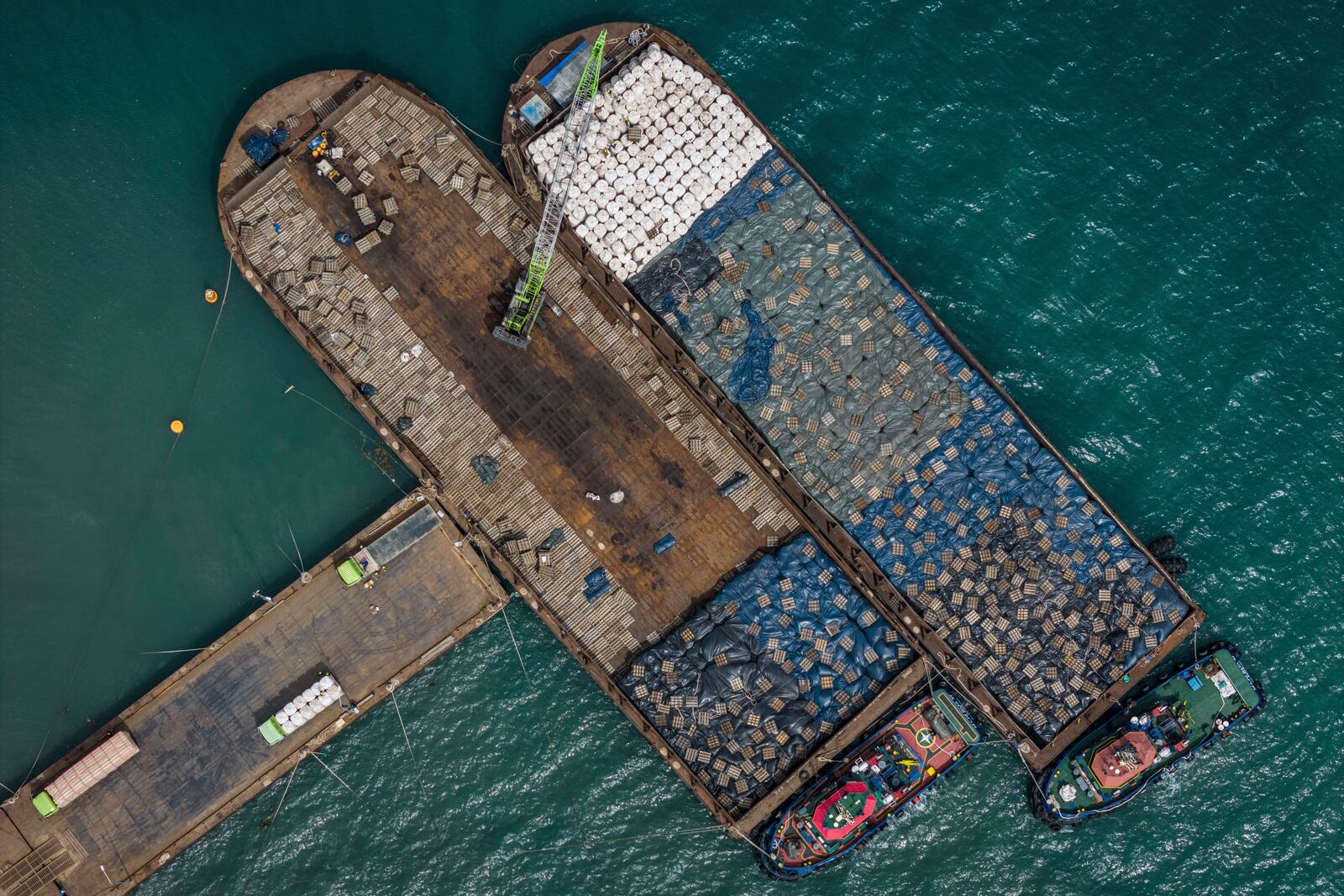 Workers load sacks of wood pellets onto barges at a port in Pohuwato, Gorontalo province, Indonesia, Tuesday, Oct. 22, 2024. (AP Photo/Yegar Sahaduta Mangiri)