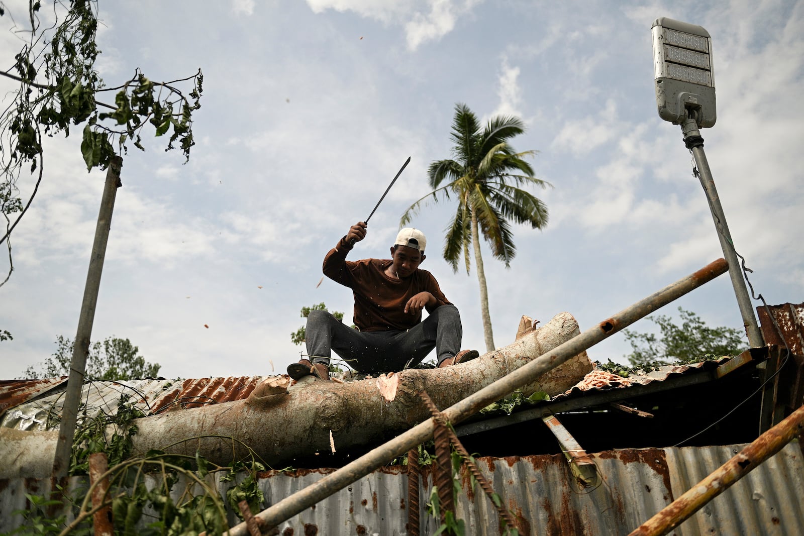 A man tries to clear a tree trunk after it fell on the roof of his house after Typhoon Yinxing, locally called Marce, blows past in Gattaran, Cagayan province, northern Philippines on Friday Nov. 8, 2024. (AP Photo/Noel Celis)