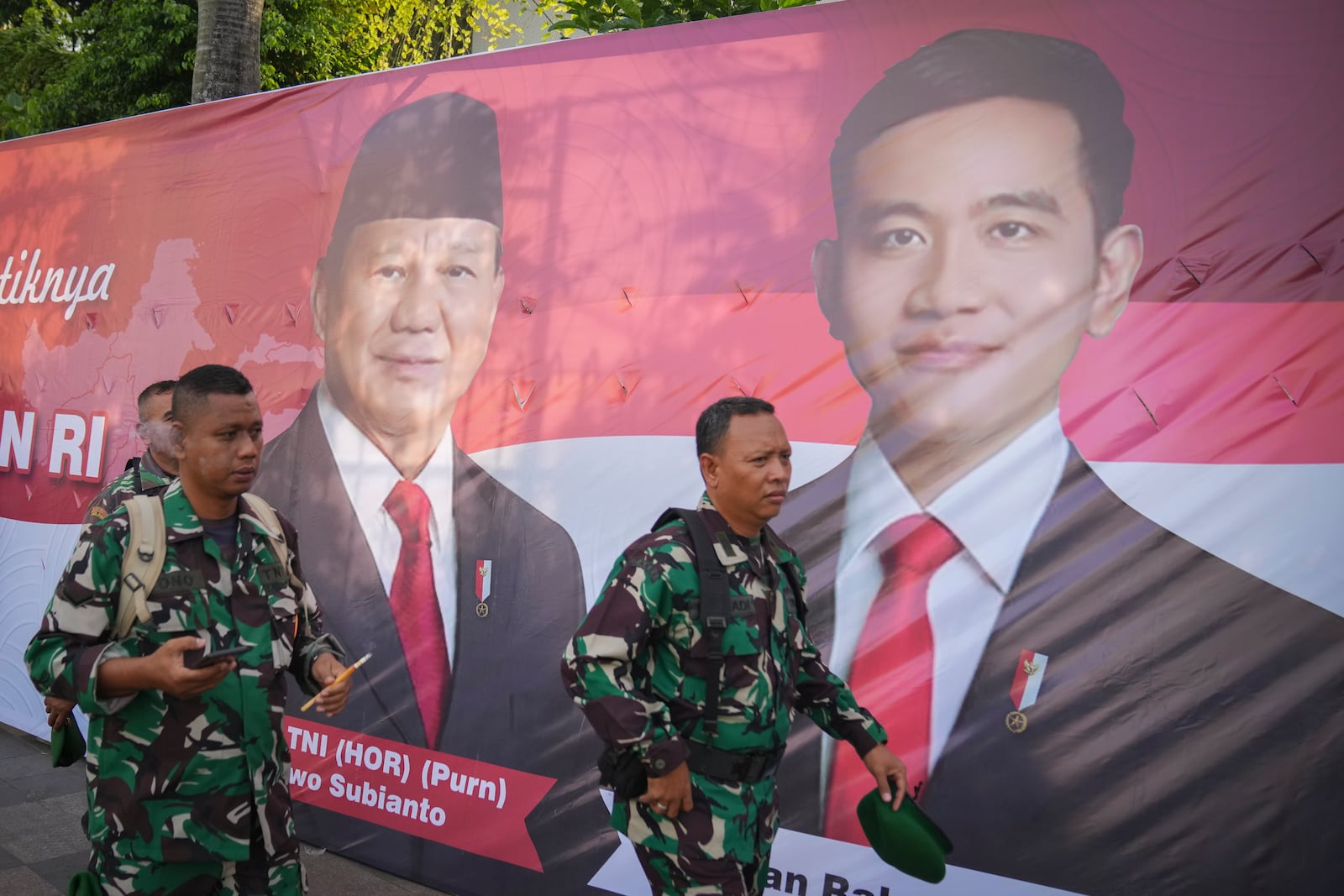 Soldiers walk in front of a banner showing Indonesian President-elect Prabowo Subianto, left, and Vice President-elect Gibran Rakabuming Raka, who is also the eldest son of outgoing President Joko Widodo, in Jakarta, Indonesia, Sunday, Oct. 20, 2024. (AP Photo/Dita Alangkara)