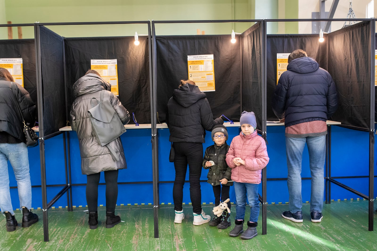 A children stand near a voting booth during the first round of voting in parliamentary election, in Vilnius, Lithuania, Sunday, Oct. 13, 2024. (AP Photo/Mindaugas Kulbis)