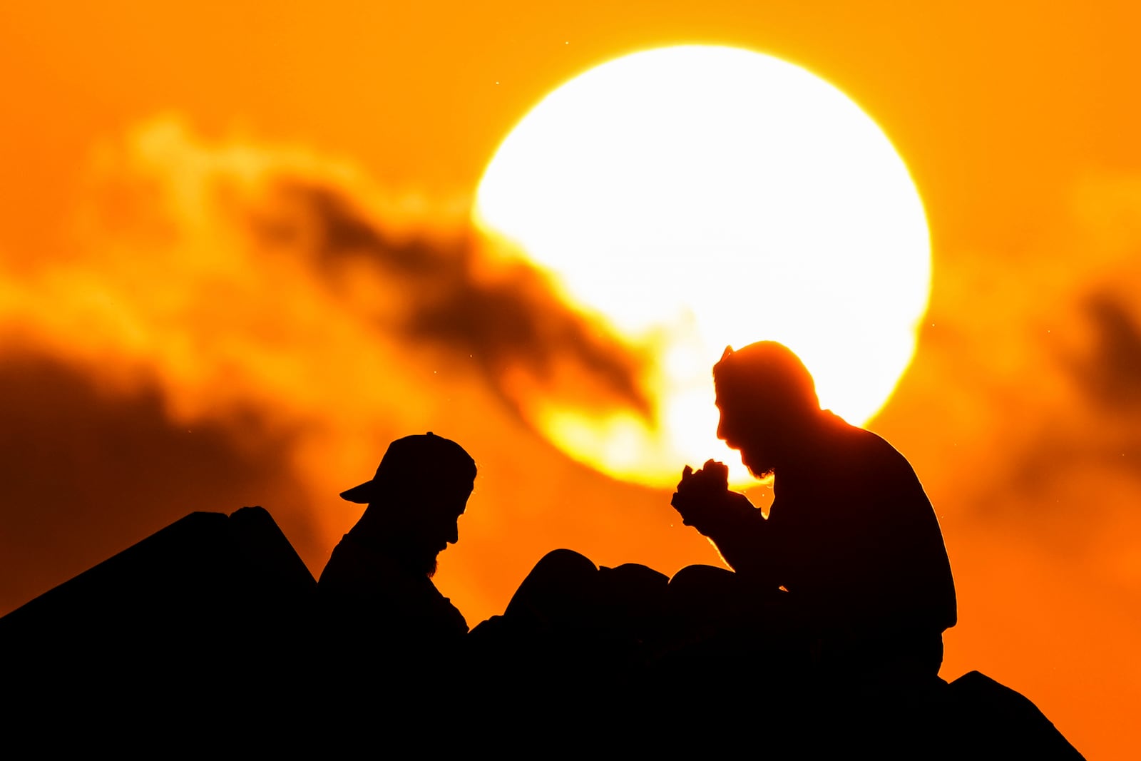 Displaced men fleeing the Israeli airstrikes in Beirut's Dahiyeh suburb, eat as sit at Beirut's seaside promenade, along the Mediterranean Sea while the sun sets over the capital Beirut, Lebanon, Thursday, Oct. 17, 2024. (AP Photo/Hassan Ammar)