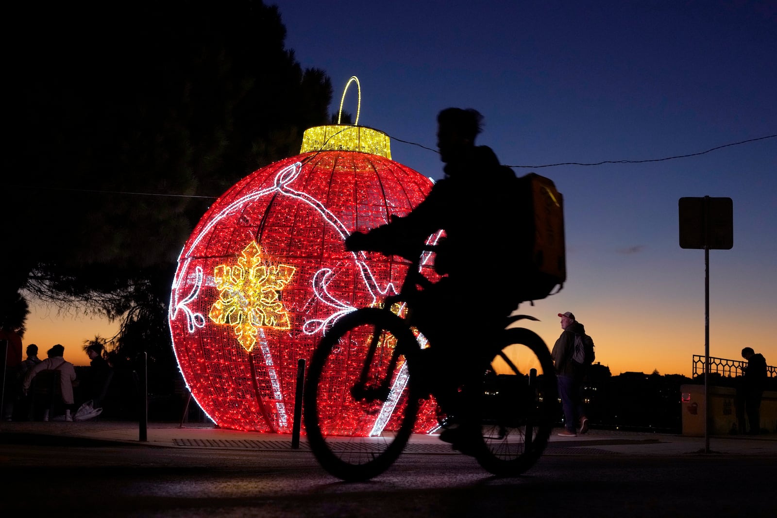 A delivery rider cycles past Christmas decorations in Lisbon, Tuesday, Dec. 24, 2024. (AP Photo/Armando Franca)