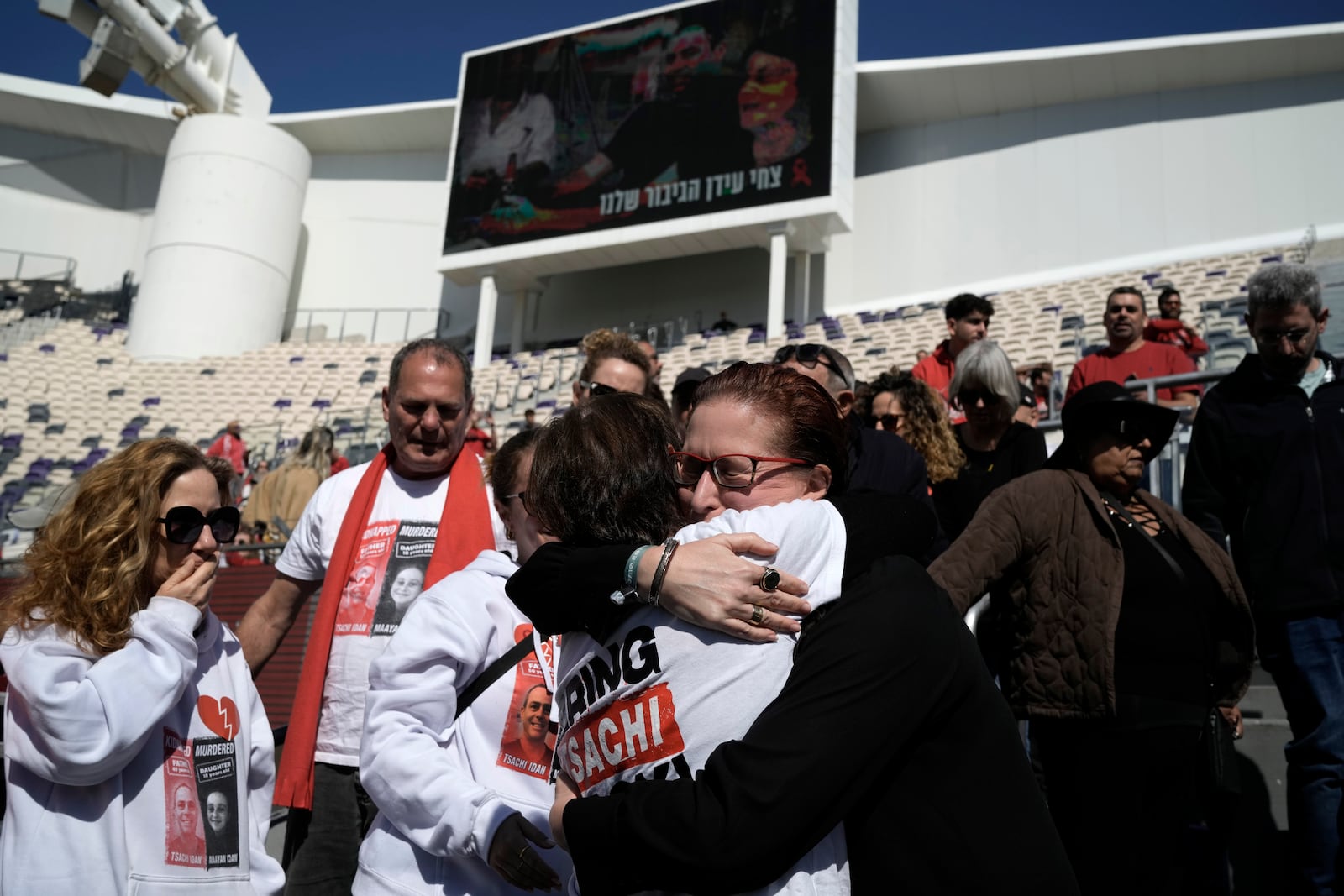 Mourners embrace at a public memorial ceremony for slain hostage Tsachi Idan, a fan of Hapoel Tel Aviv F.C., who was killed in Hamas captivity in the Gaza Strip, at Bloomfield Stadium in Tel Aviv, Israel, Friday, Feb. 28, 2025. (AP Photo/Leo Correa)