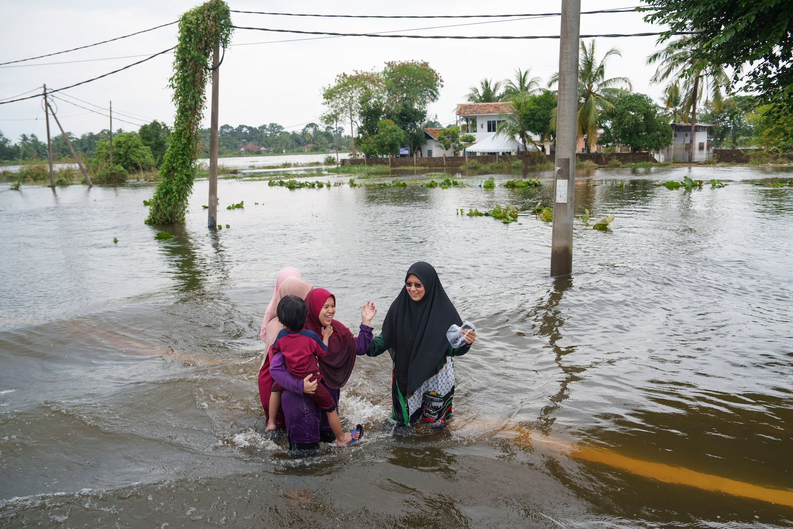 People wade through flood waters in Tumpat, outskirts of Kota Bahru, Malaysia, Tuesday, Dec. 3, 2024. (AP Photo/Vincent Thian)