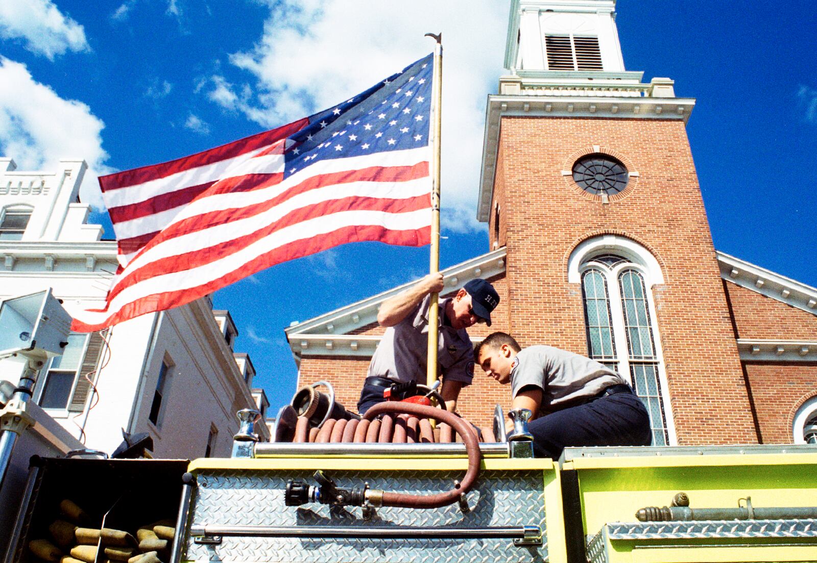 Greg Lynch/Journal-News
Hamilton firefighters Mike Lewis and Grant Cruxton hoist the American flag atop thier engine truck Friday outside The Presbyterian Church on Front St.